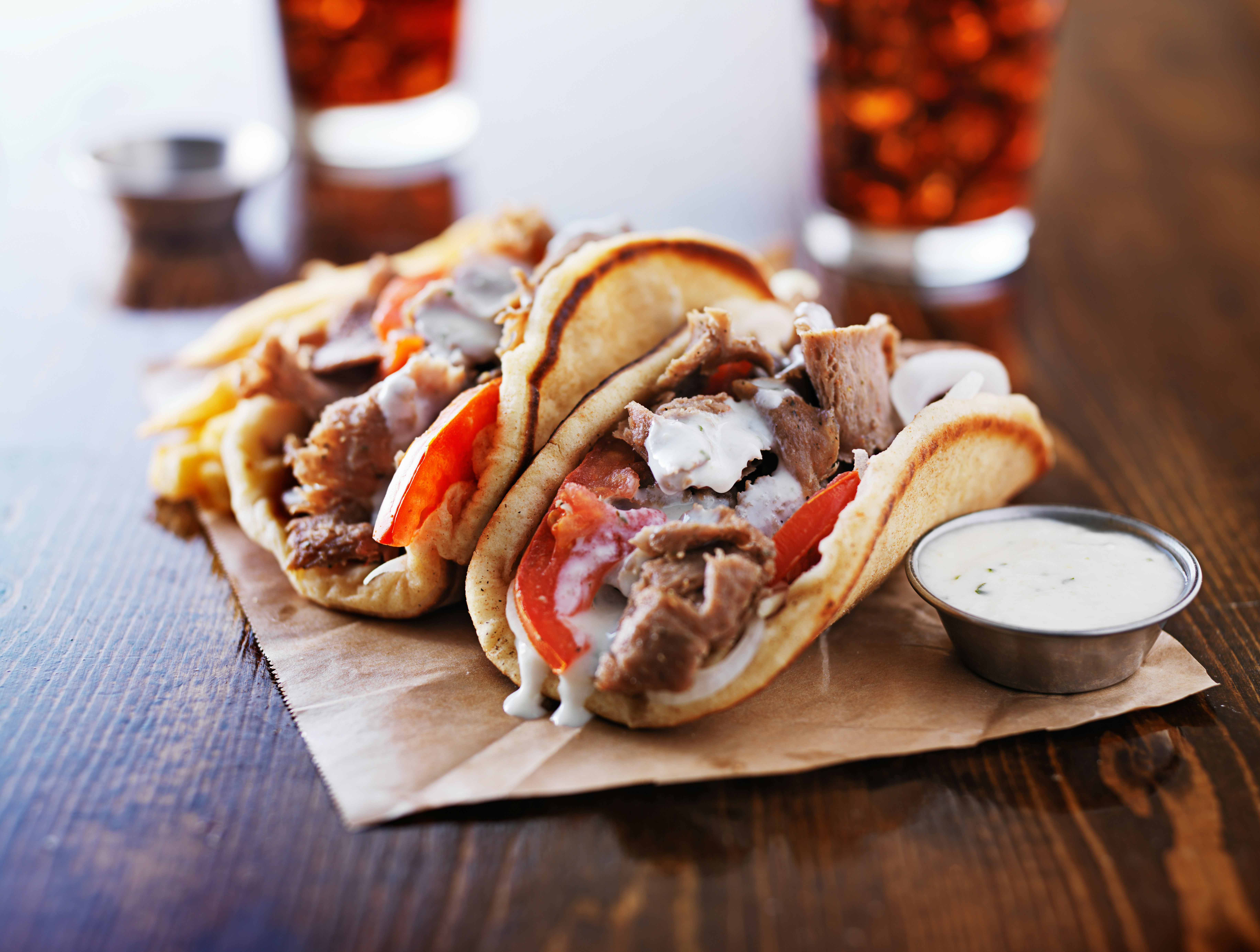 Greek gyros served with tzatziki sauce and fries on a wooden table with two glasses of cola in the background.