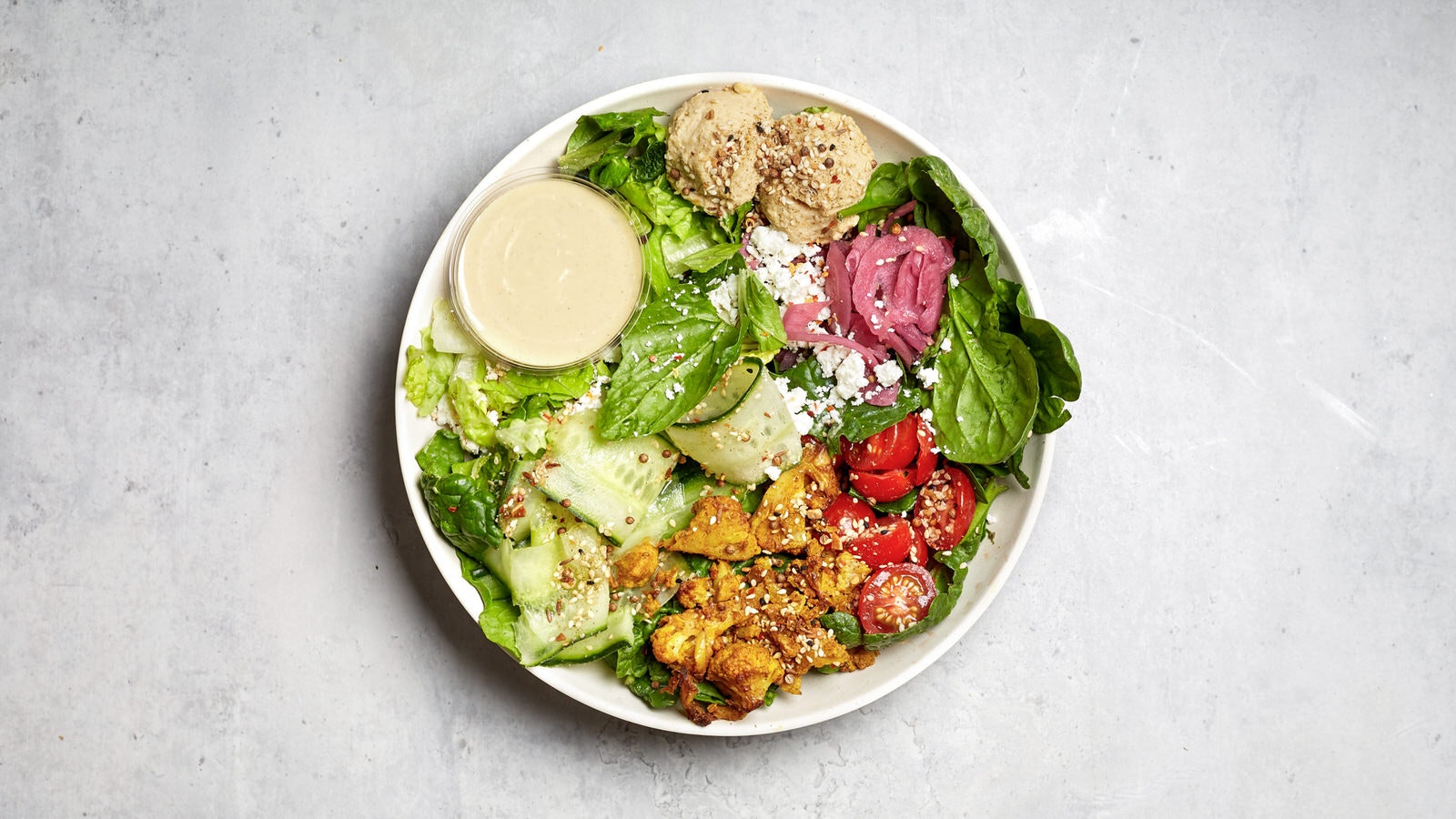A vinbrant salad bowl with spinach, cucumber, feta, red onion, cherry tomatoes, cauliflower, hummus, dukkah and tahini yoghurt dressing from Atis in Shoreditch