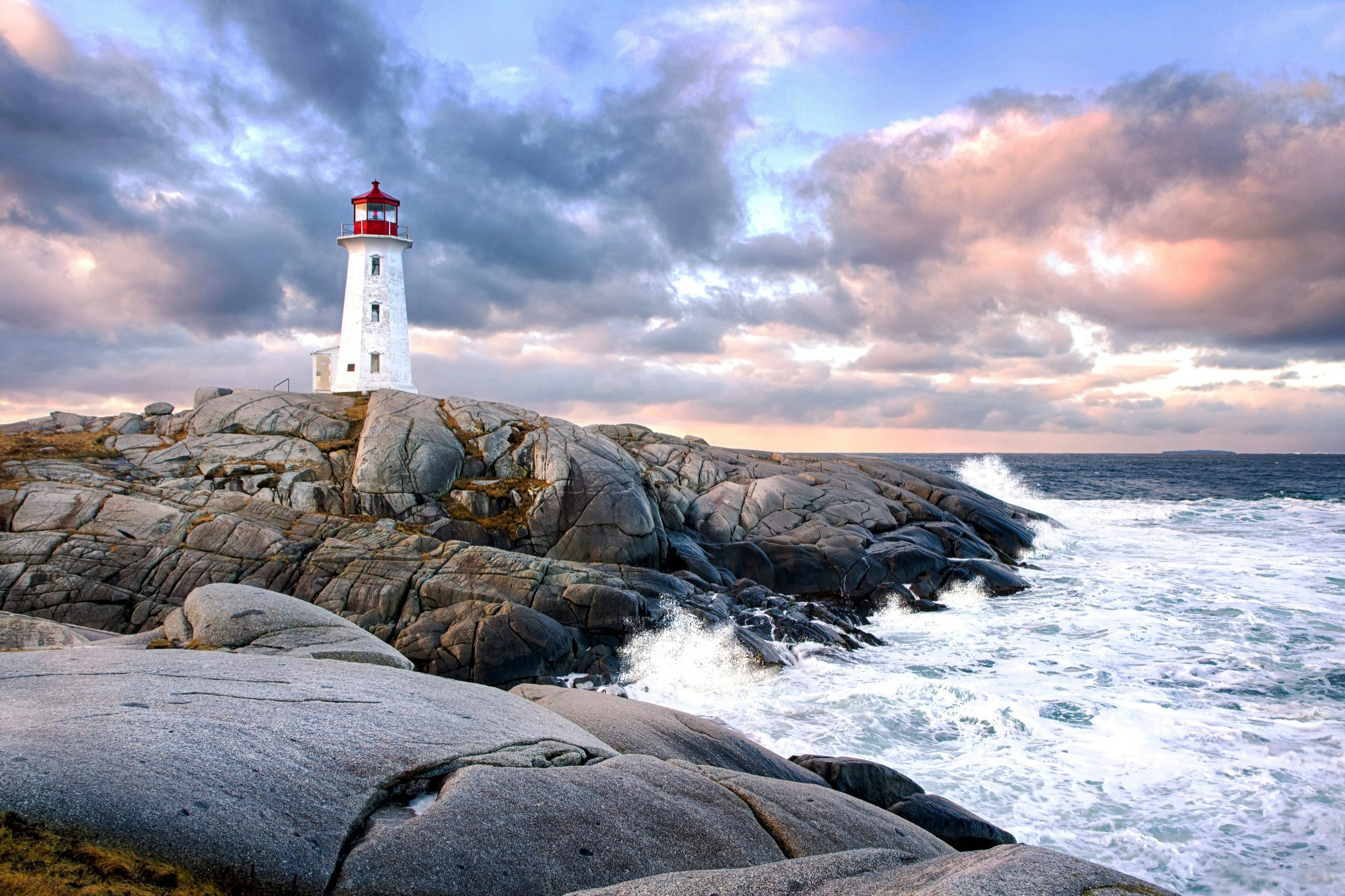 Waves crash on the rocks below a red and white lighthouse near Halifax, Nova Scotia
