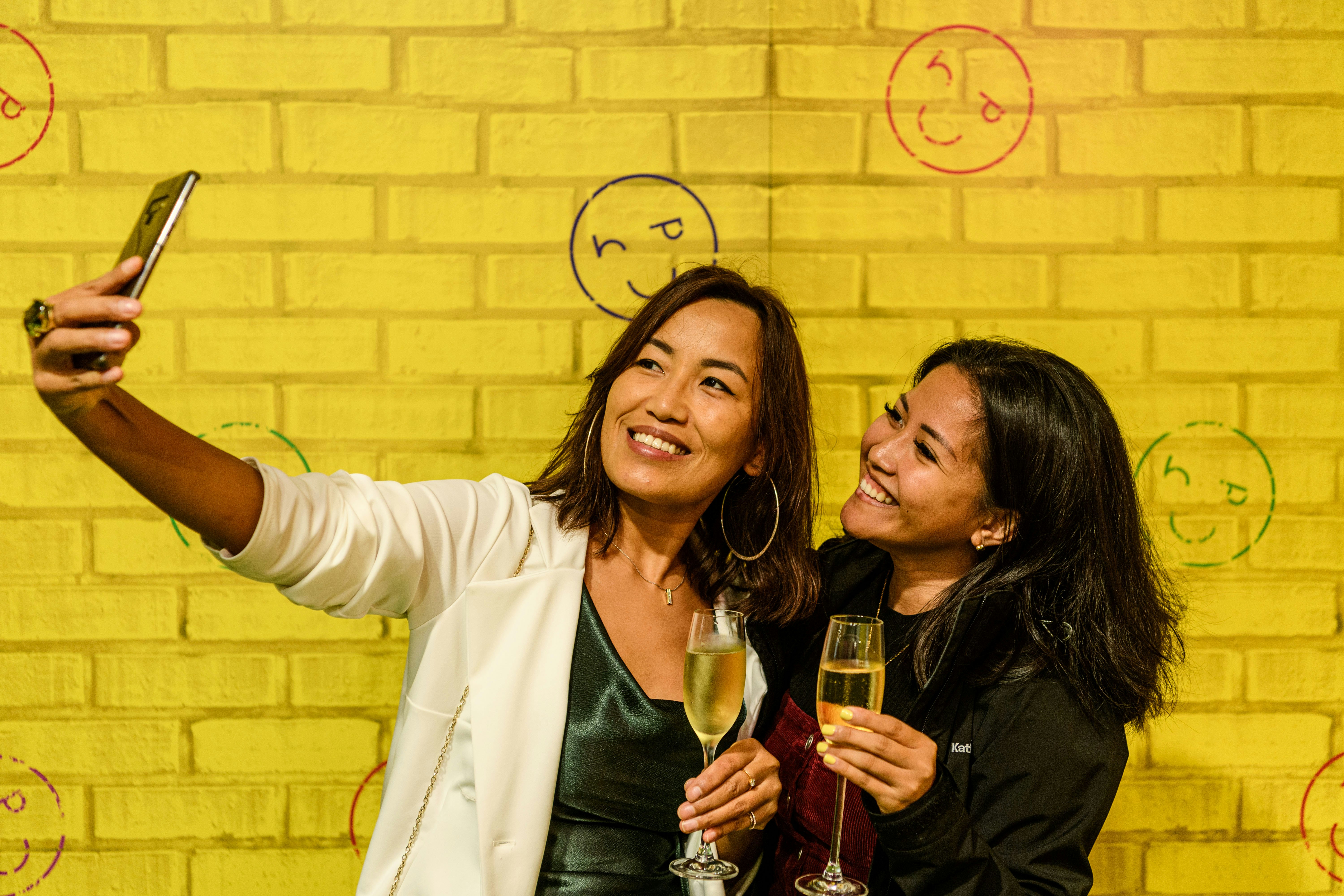 Two young women take a selfie against a bright yellow backdrop