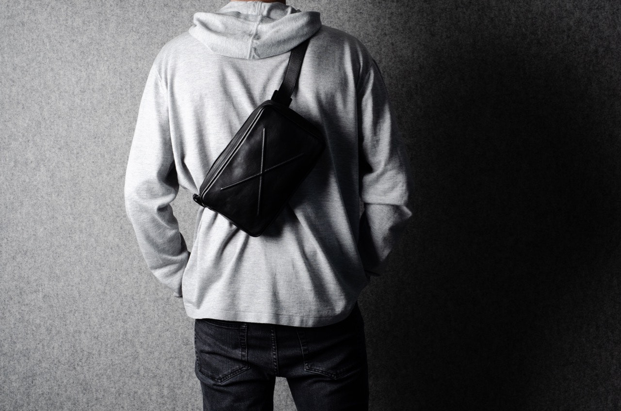 A person dressed in a grey sweatshirt, wearing Hardgraft's phone pack across his back