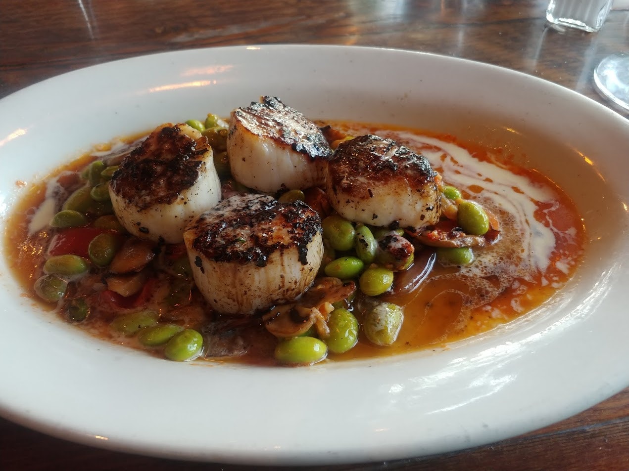 A white dish of seared scallops in a red sauce with bright green edamame at Harvey's restaurant in Ashland Oregon