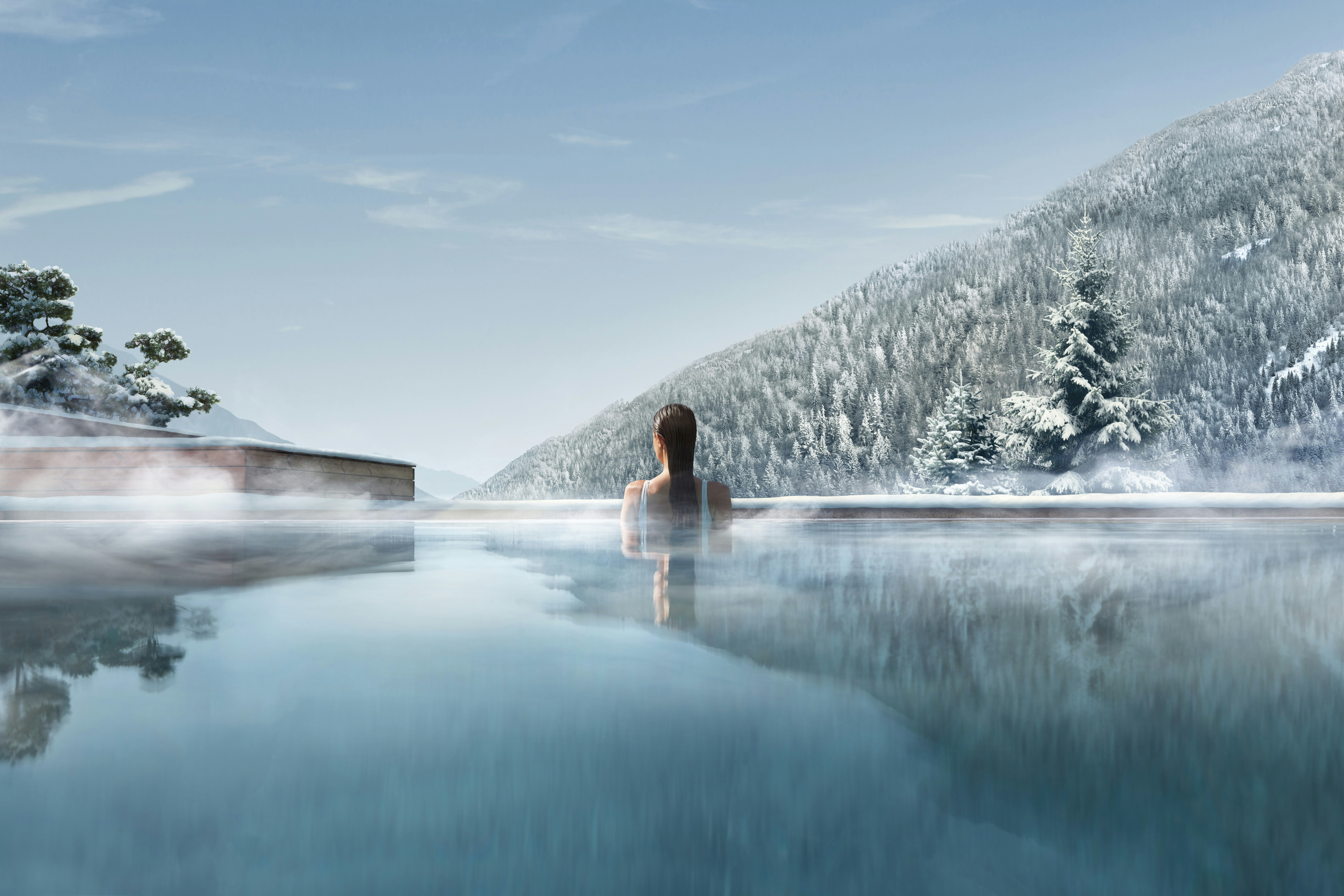 A woman in an outdoor pool in Italy, looks on over an icy forest. A light mist is over the water