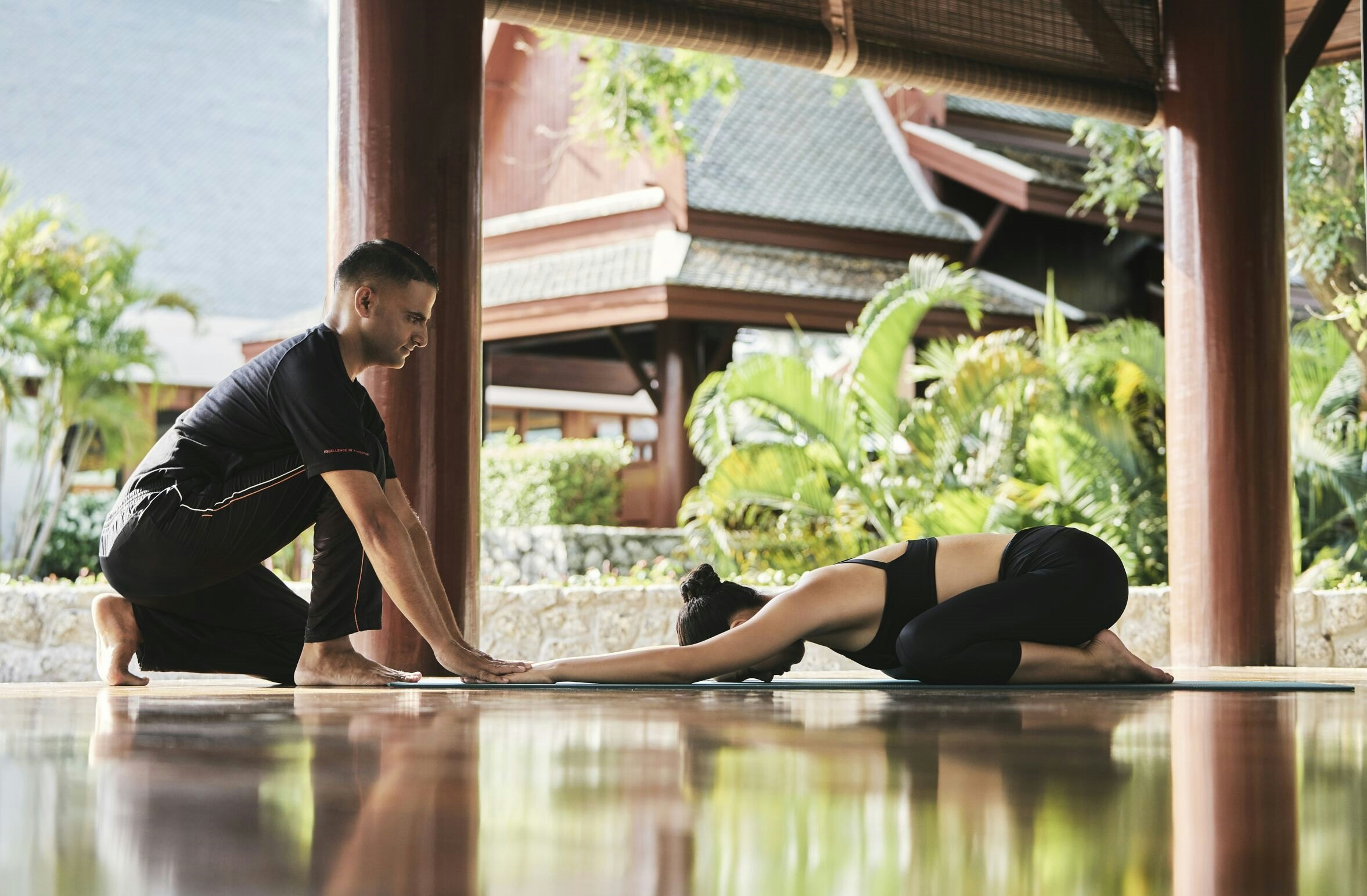 A woman poses for yoga with assistance from her instructor, in Thailand