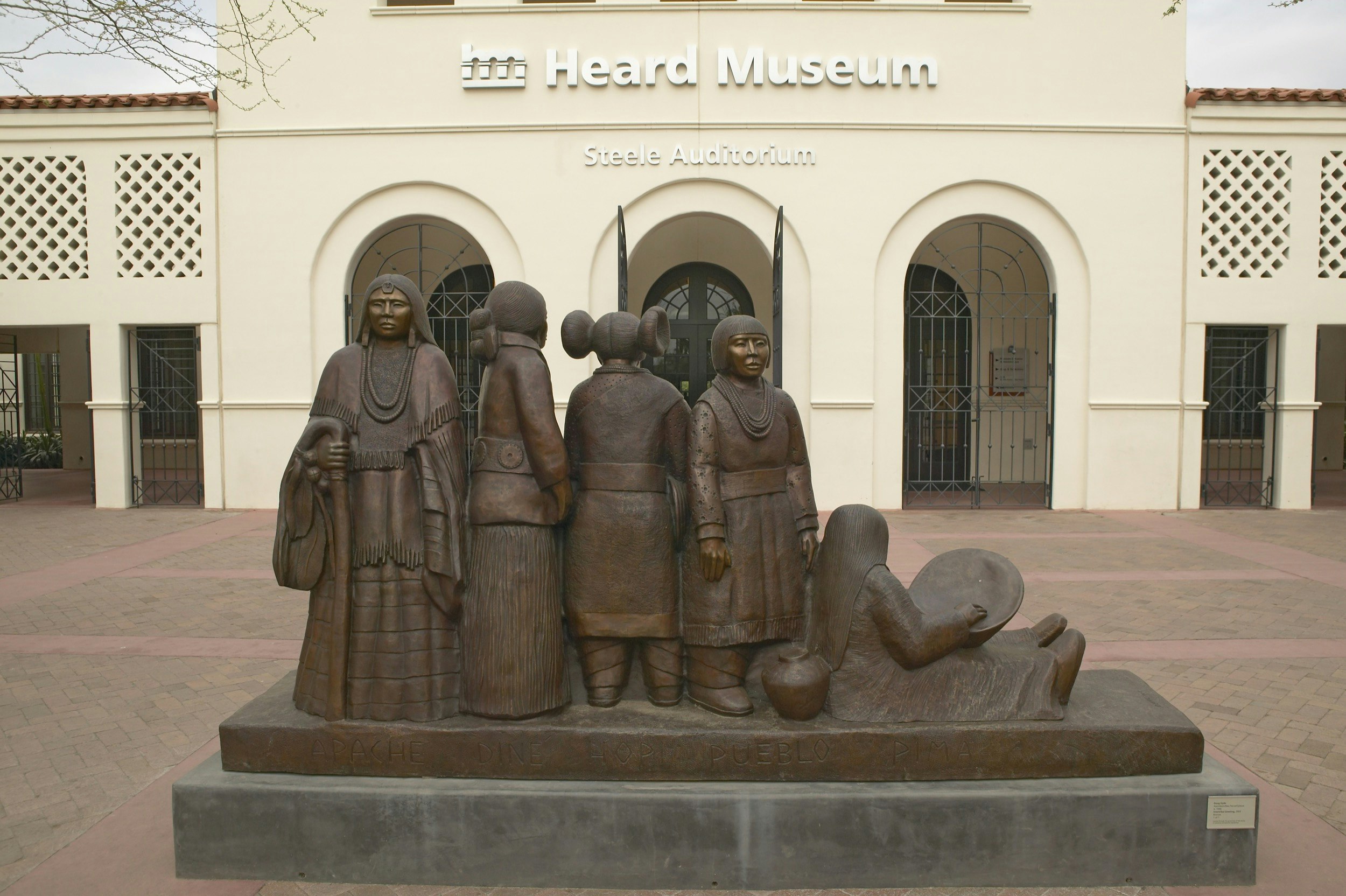 A statue featuring four Native American women stands in front of the entrance to the Heard Museum