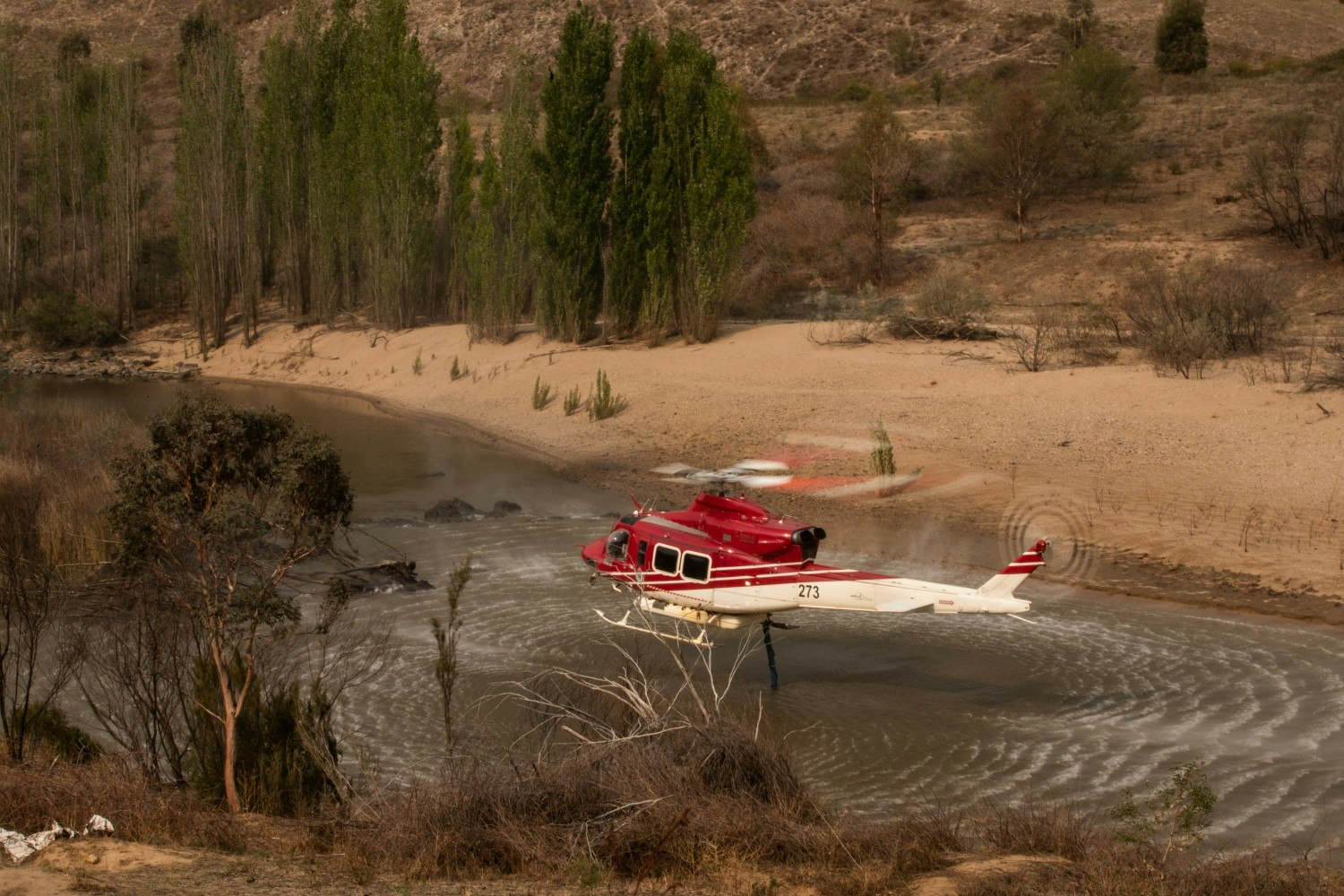 A water bombing helicopter picks up water as fire creeps forward in Namadgi National Park  