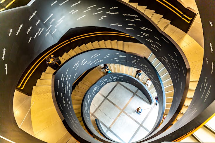A winding stair in the interior of the New Helsinki city library, which is called Oodi. People are walking up and down the stair, and writing is visible on its inside. 