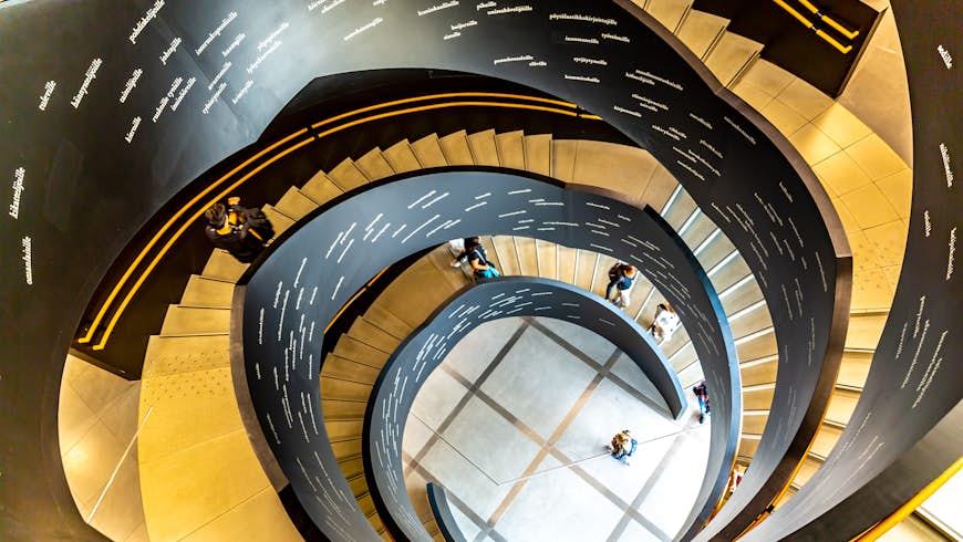 A winding stair in the interior of the New Helsinki city library, which is called Oodi. People are walking up and down the stair, and writing is visible on its inside.