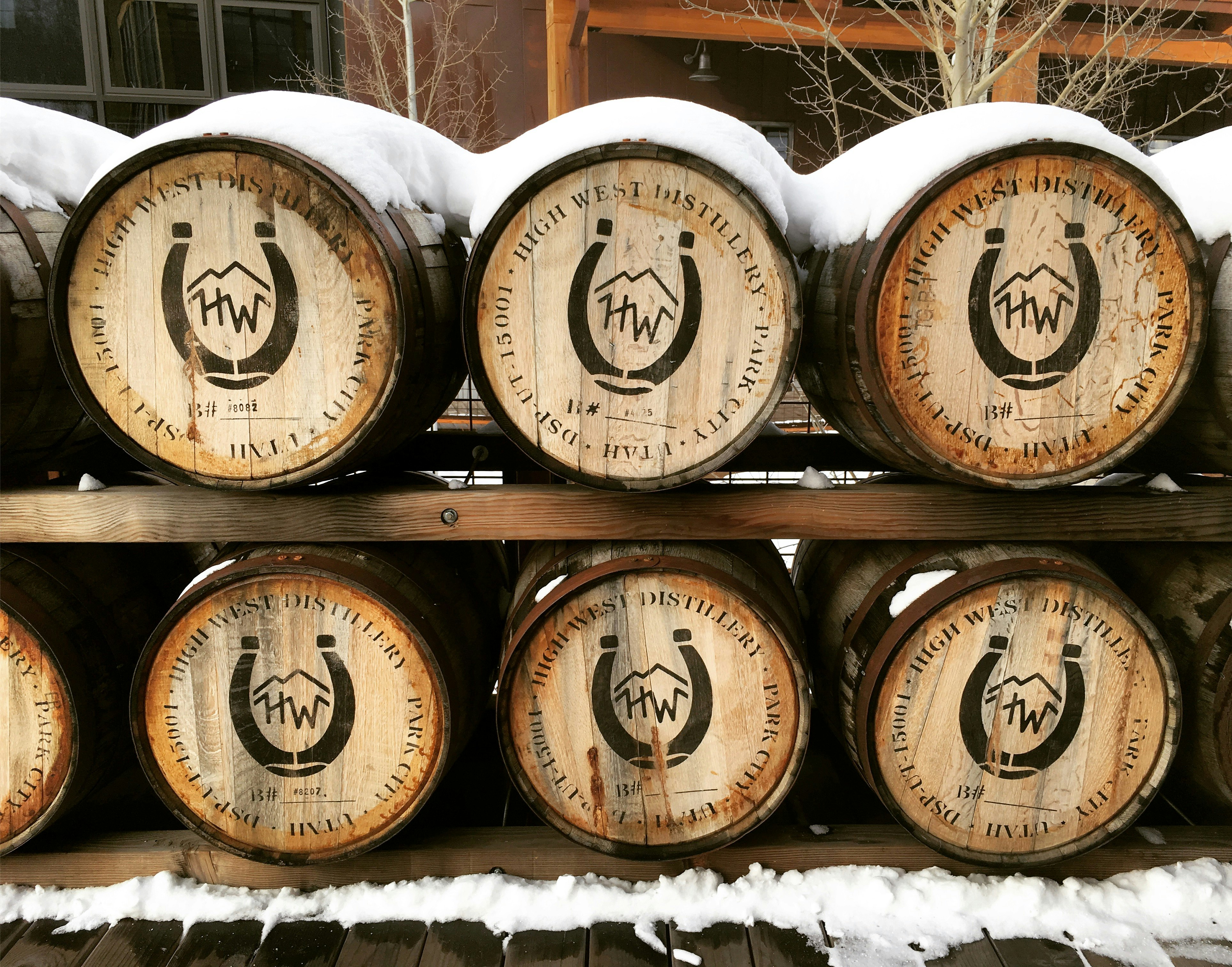 Two rows of wooden barrels are shelved outside. The barrels on the top are covered with snow; unusual distilleries  