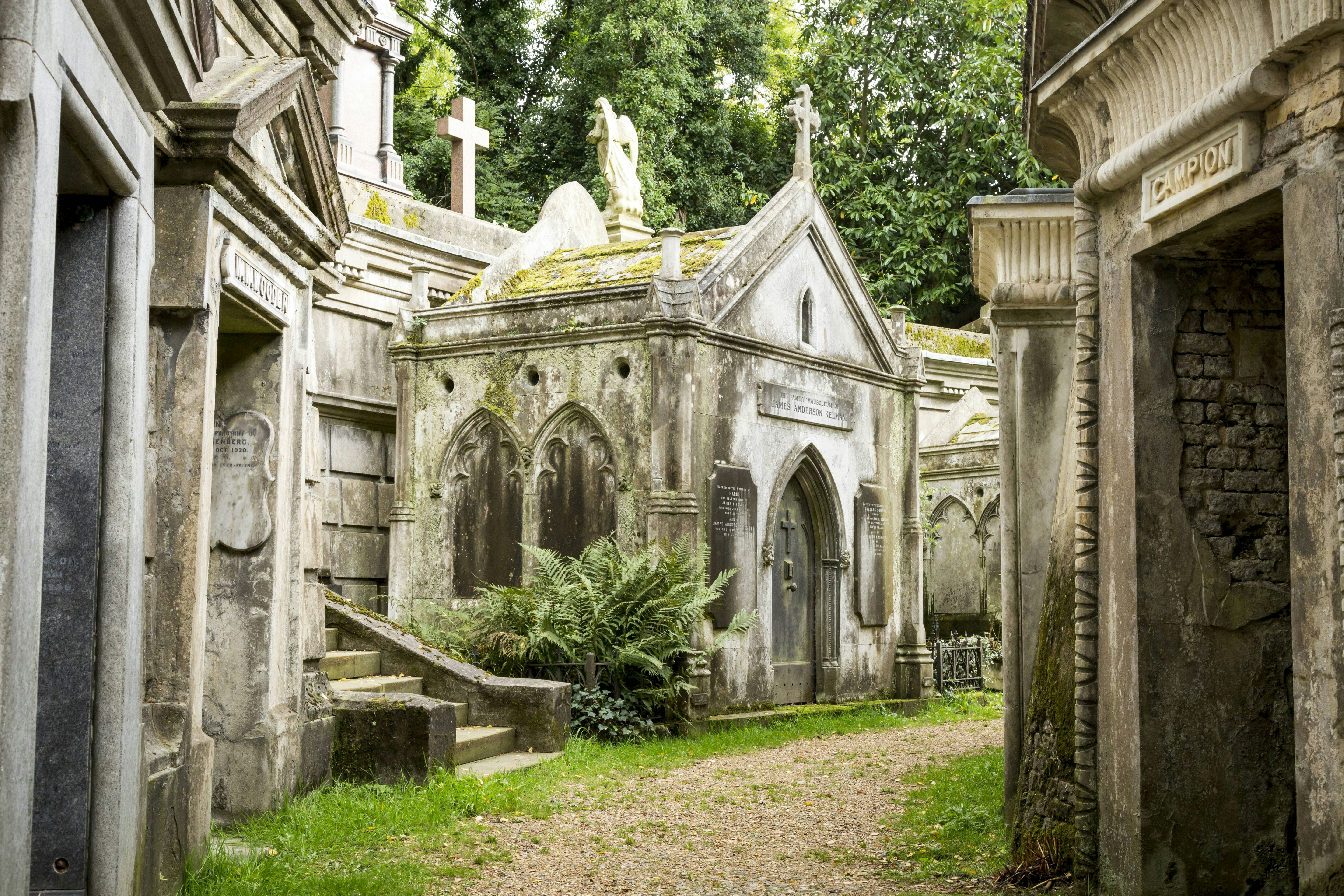 A path leading through Highgate Cemetery in London. There are large tombs running alongside the path.