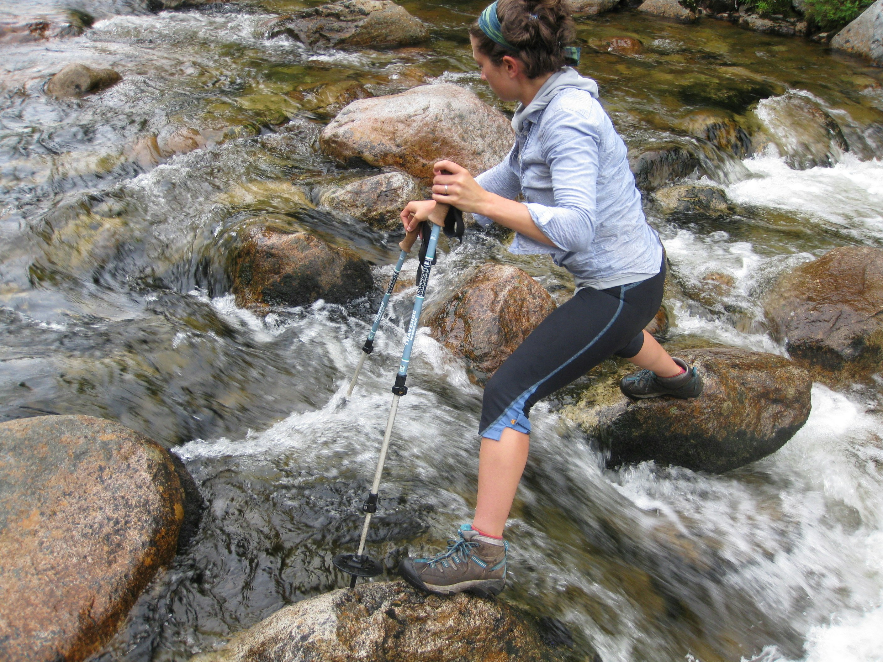 A woman uses poles to help her hike along a creek in the Maine backwoods