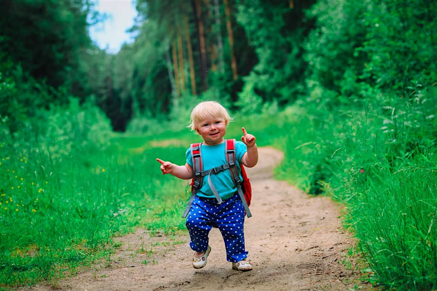 A toddler bebops down a trail with an oversized backpack on; kids outdoor activities