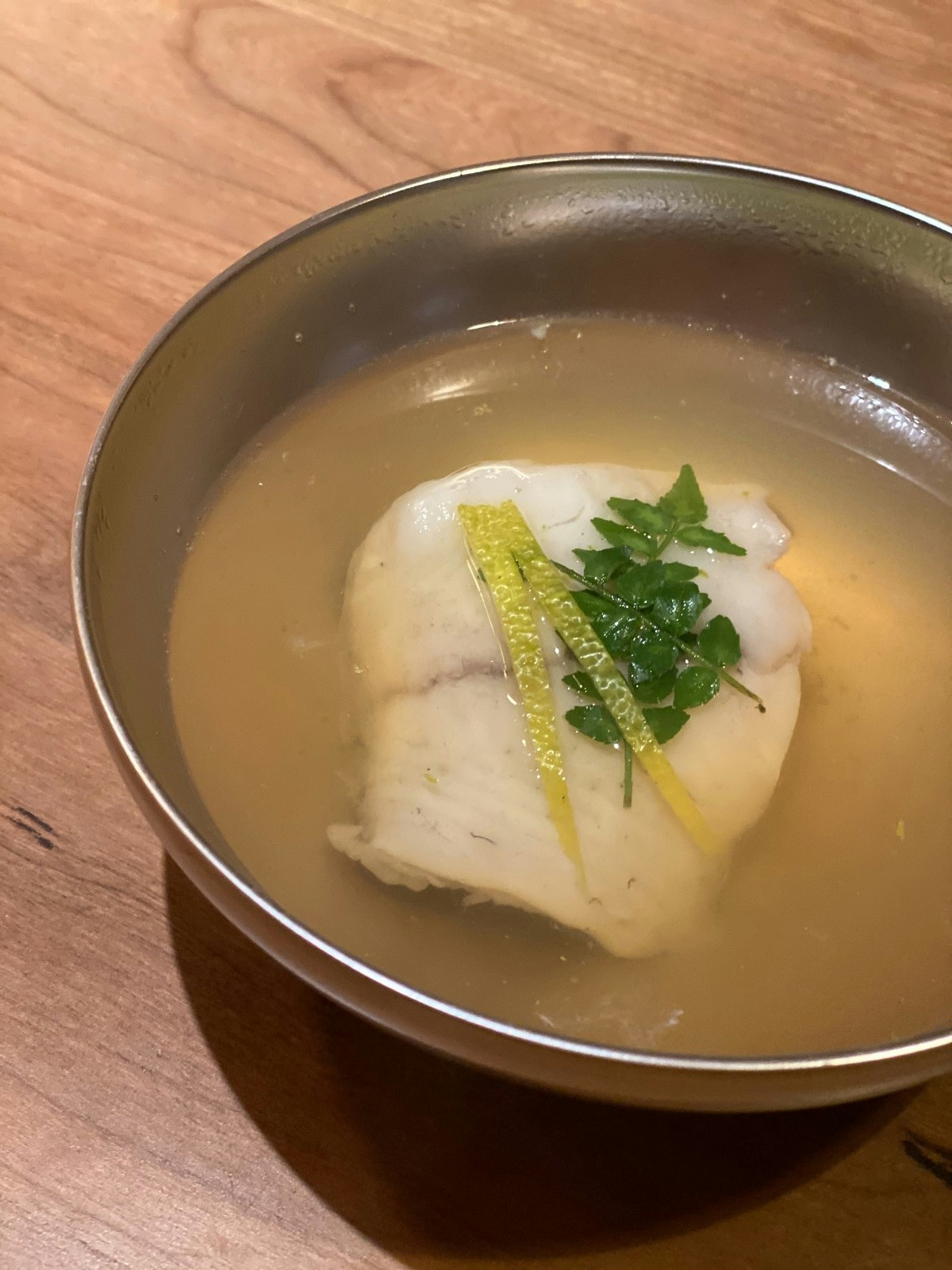 A close up of a bowl of Hirame Dashi at Sake no Hana. Turbot and citrus fruit in a clear broth.