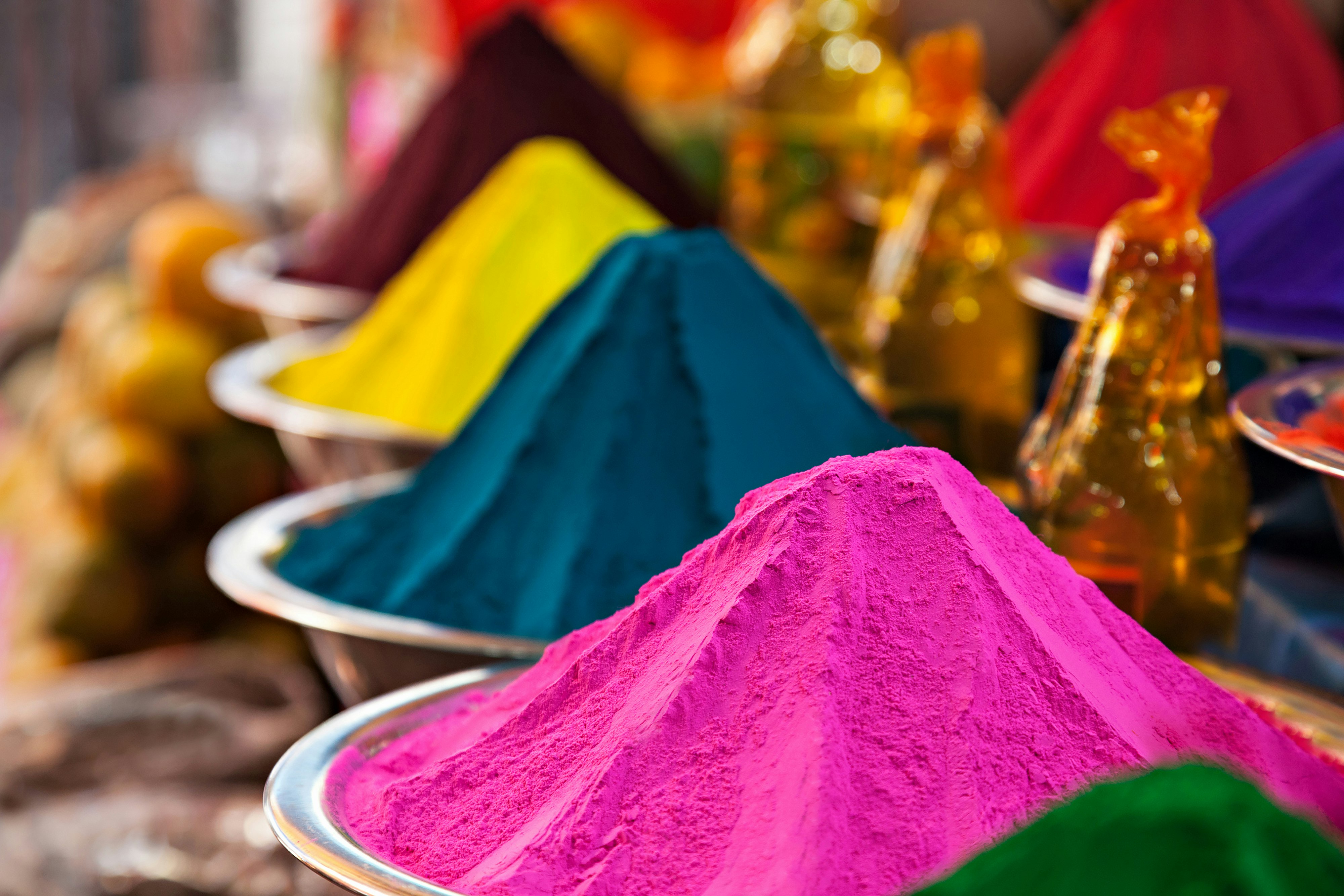Piles of coloured powders in metallic bowls are on sale in a shop in India.