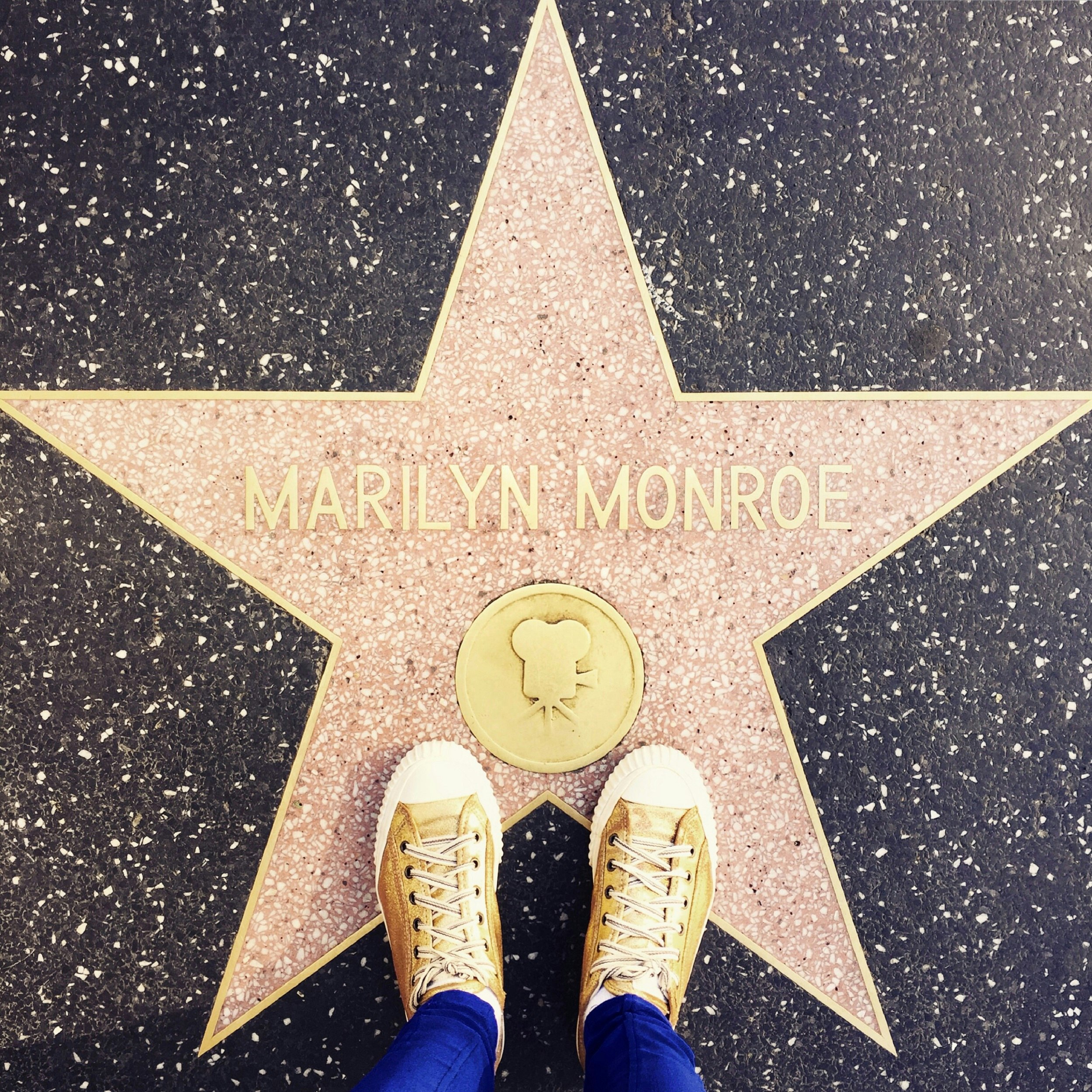 A shot from above: a person's sneakers are visible standing on the edge of the Marilyn Monroe star on the Hollywood Walk of Fame.