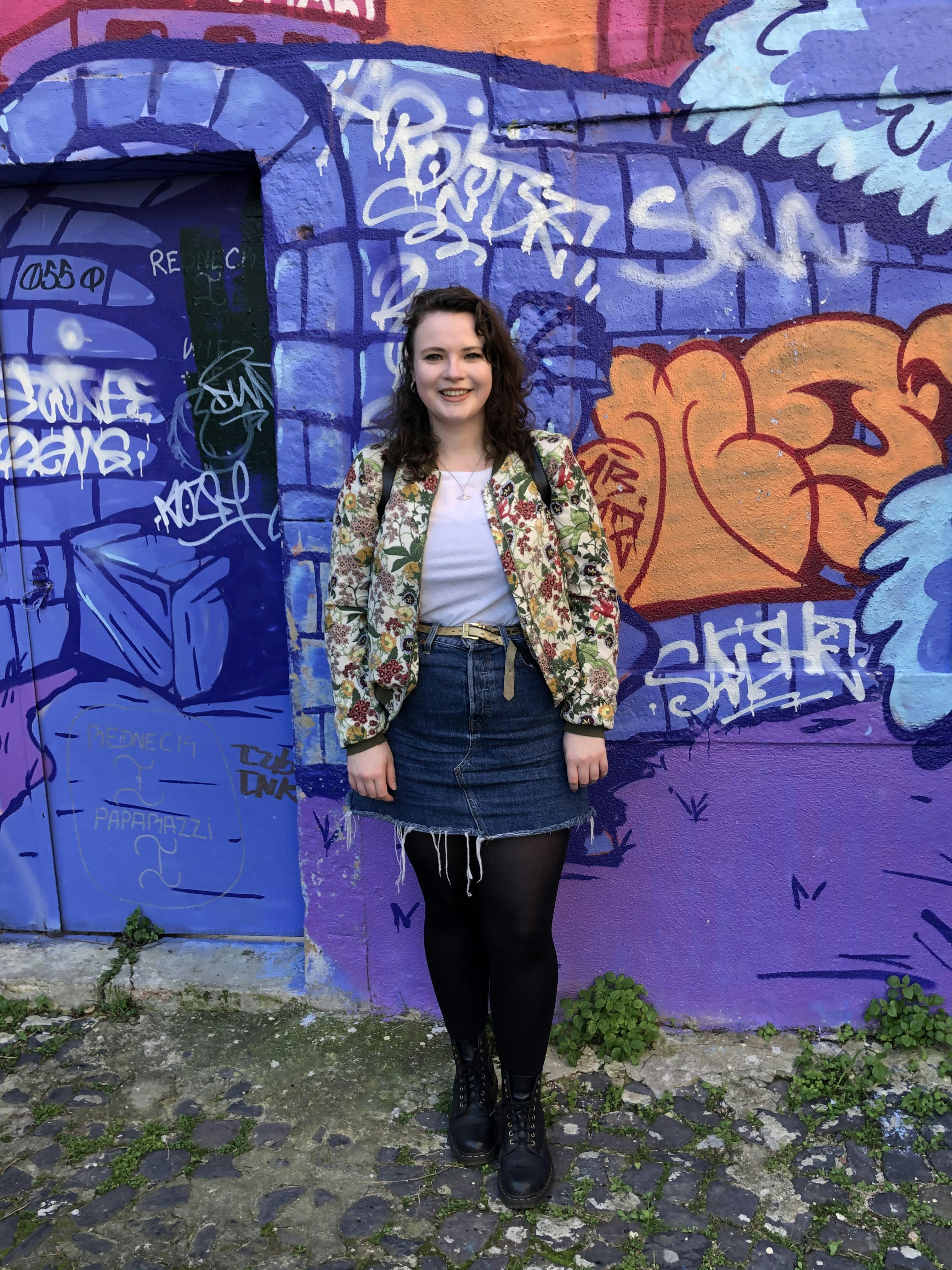 Writer Hope Brotherton poses in front of a blue wall with graffiti on it