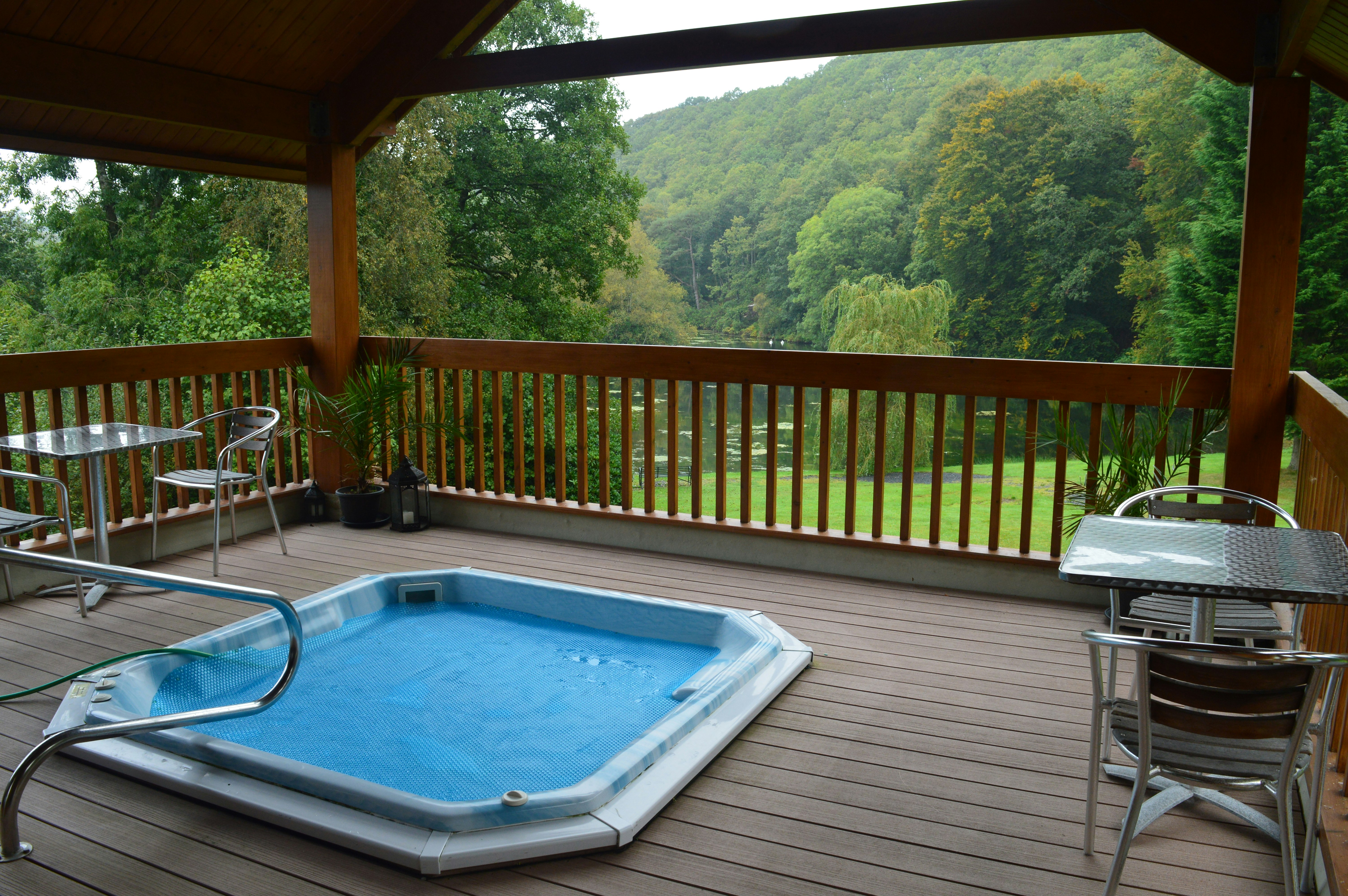 A hot tub surrounded by wooden decking and a roof with views of the countryside.