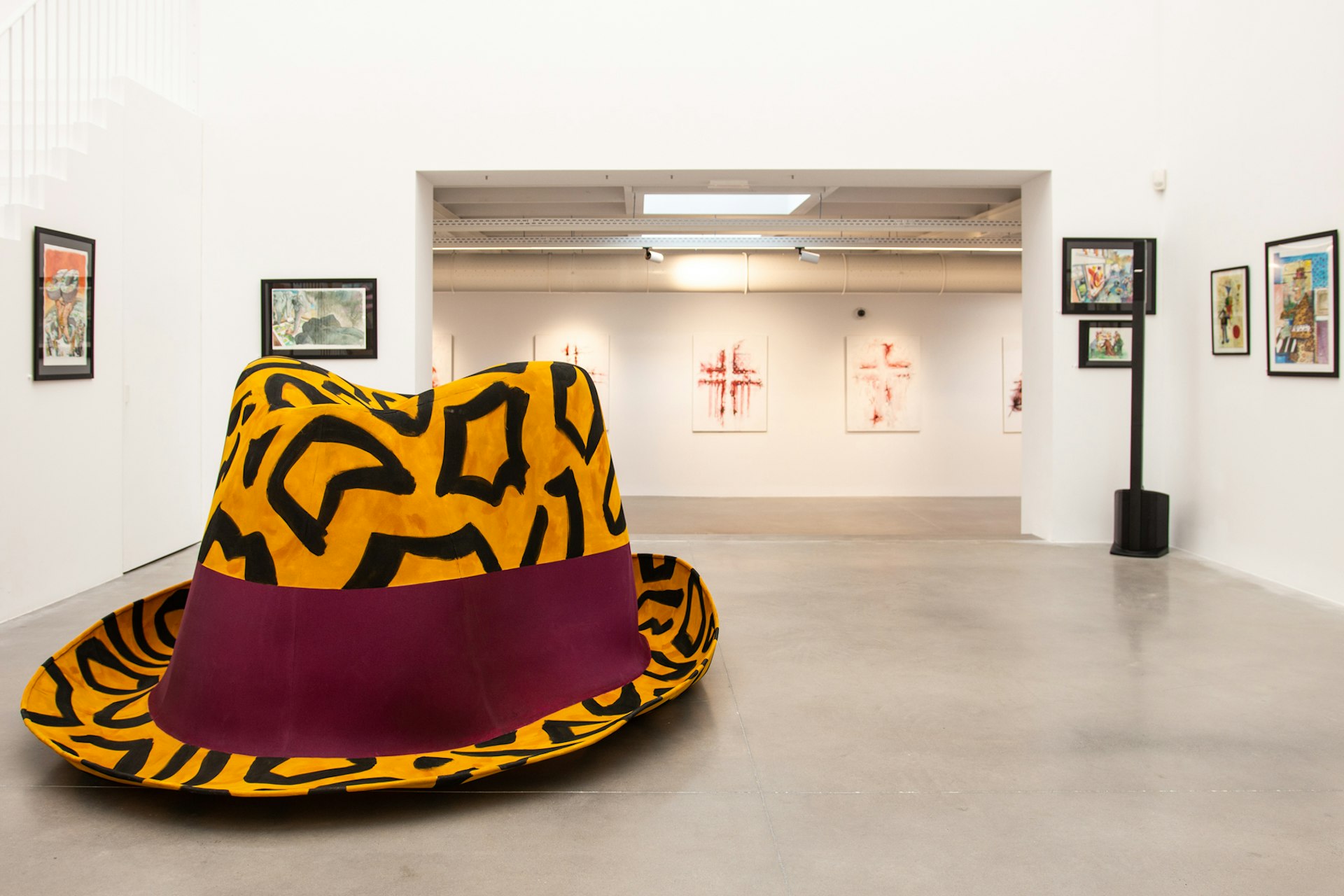 The white-walled, grey-floored interior of Huberty Breyne Gallery; in the centre of the room is a huge camel-coloured fedora with a black pattern and a purple band.
