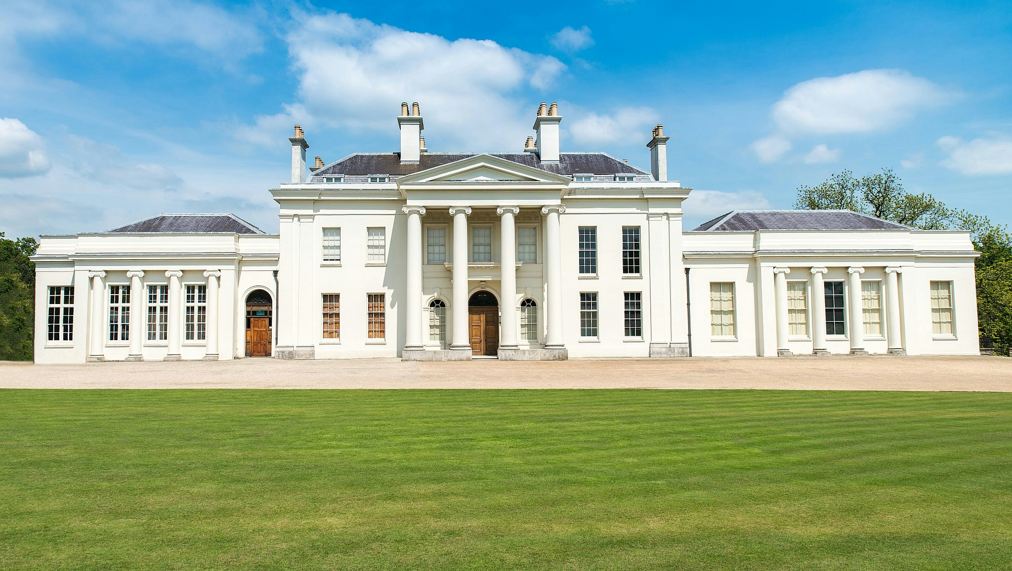 Hylands House, a white neoclassical mansion with a grey roof and a large green lawn in front of it.