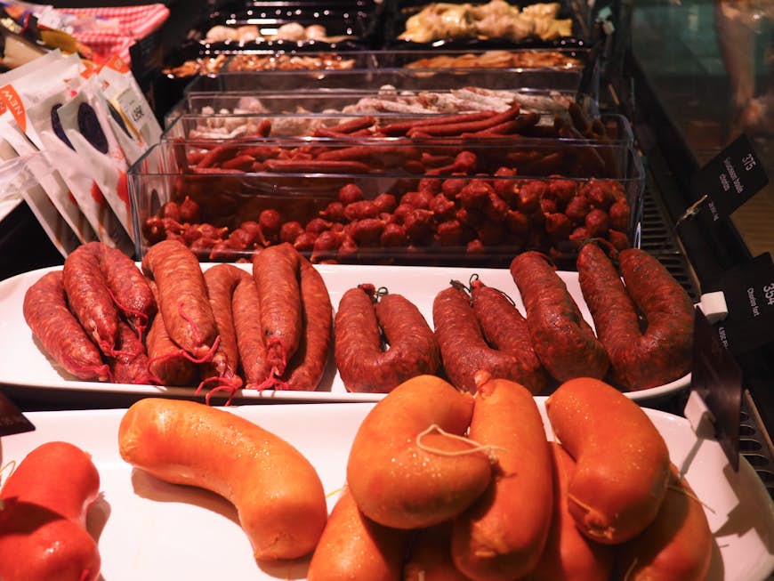 Many different types of sausage laid out on several dishes at a deli counter in Lyon