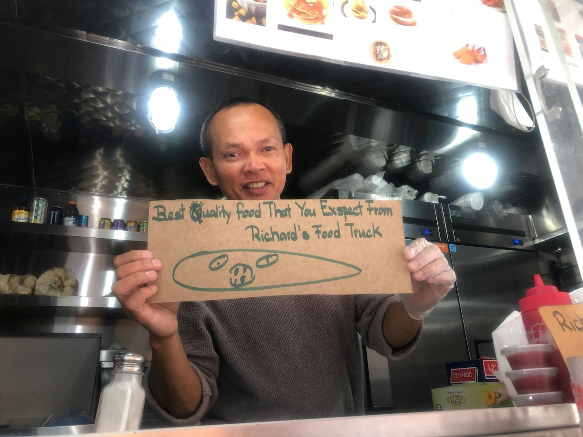 The owner of Richard's inside his truck, holding up a sign about his "best quality food" 