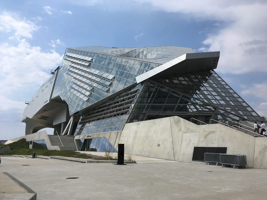The exterior of the Musée des Confluences is made of glass and steel with a concrete ramp up to the entrance. The building has an unusual shape, a little like a crouching animal