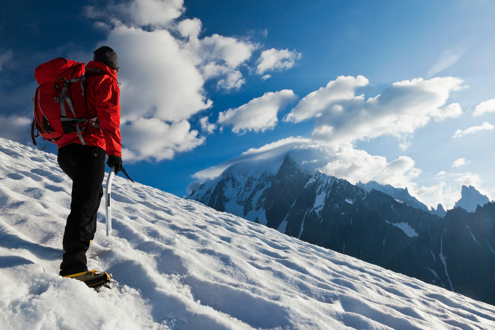 A man stands on a snowy mountain overlooking another snow-capped mountain 