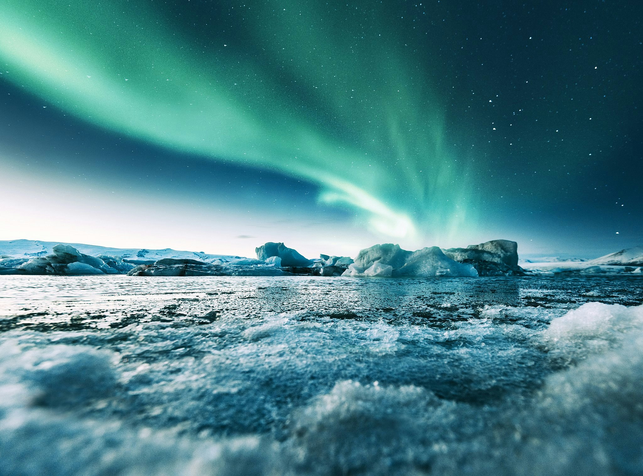 The shimmering green lights of the aurora borealis above a large icy glacial lake.