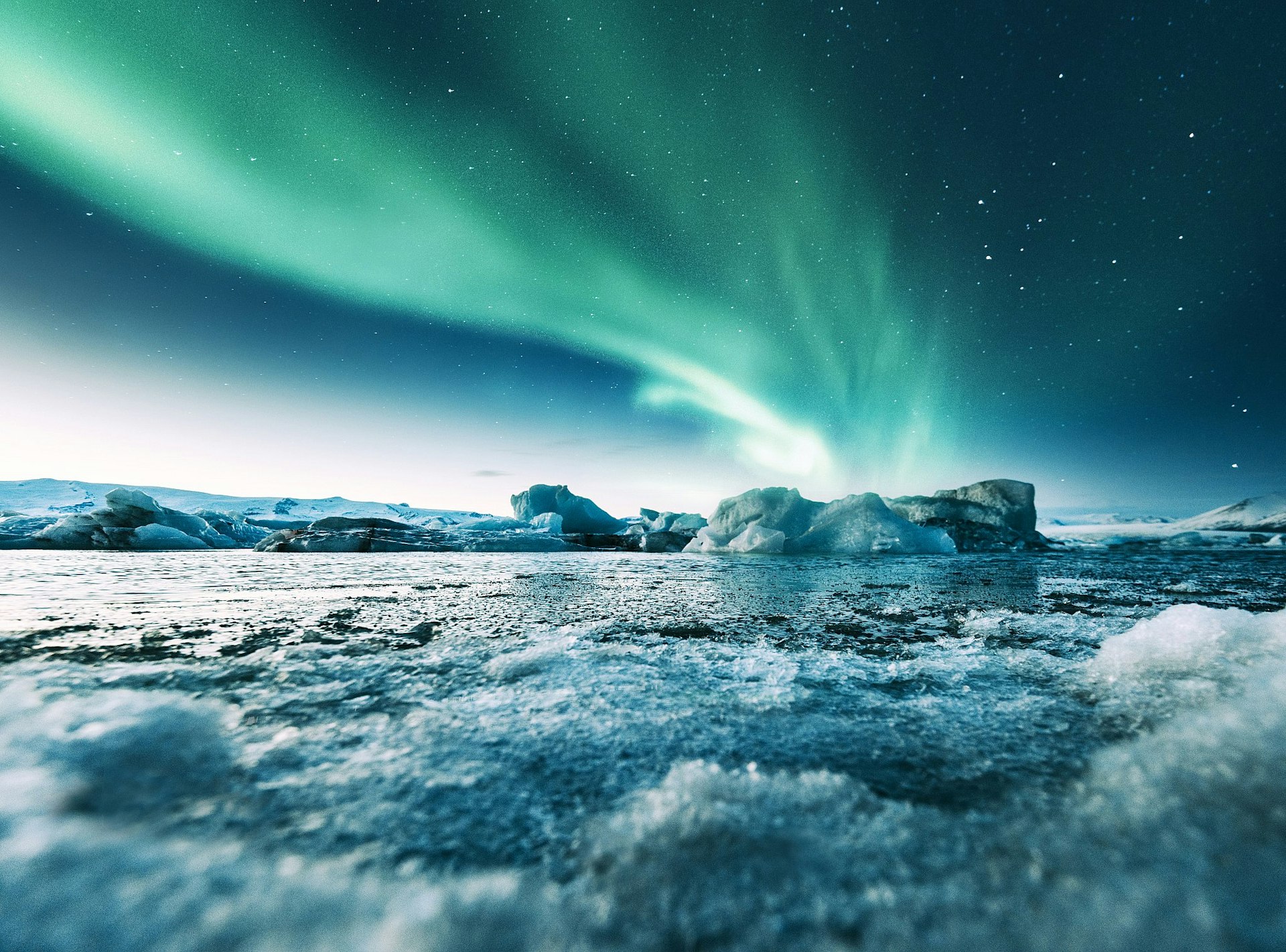 The shimmering green lights of the aurora borealis above a large icy glacial lake.