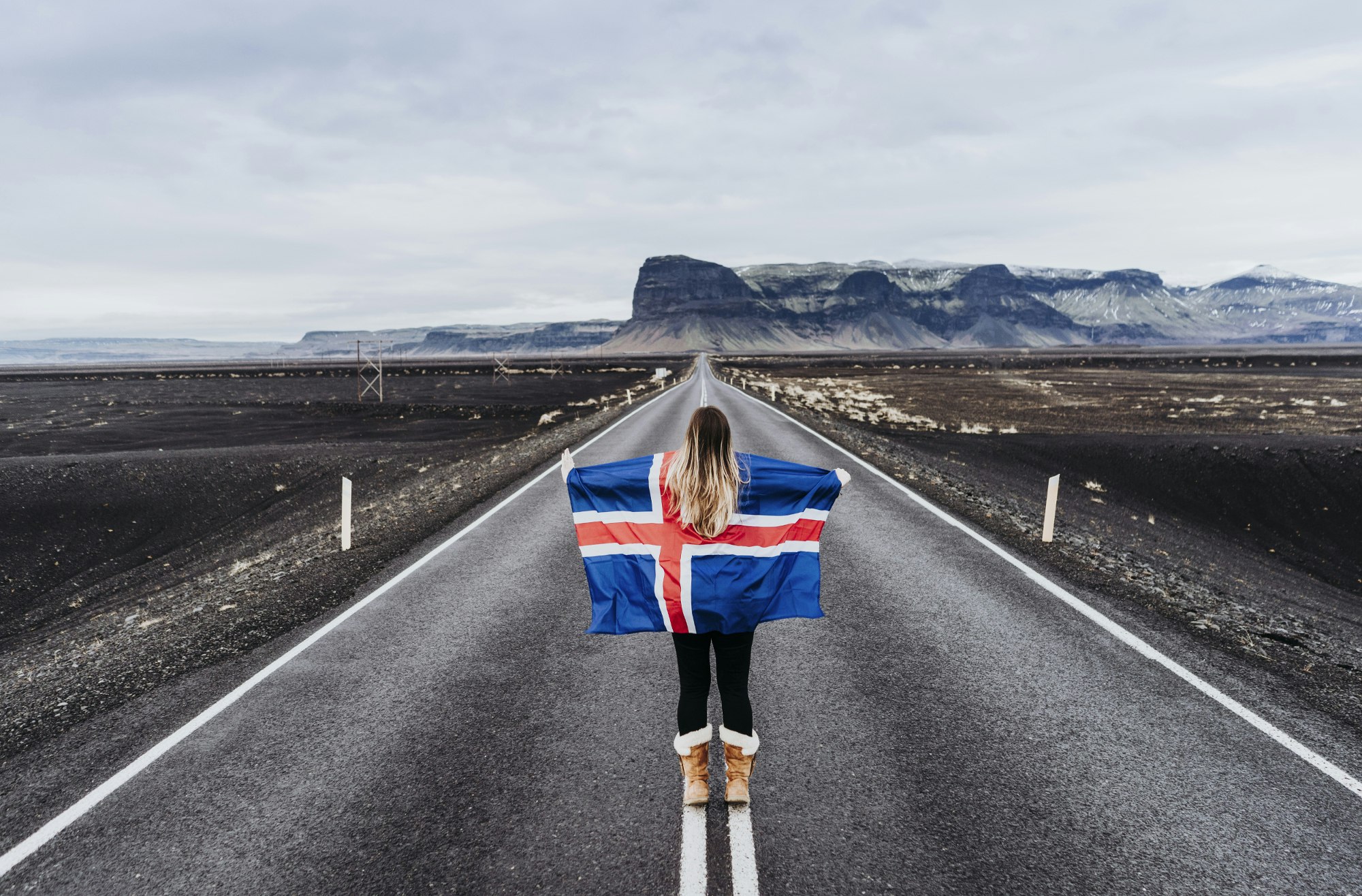 a woman holds an Icelandic flag on a road