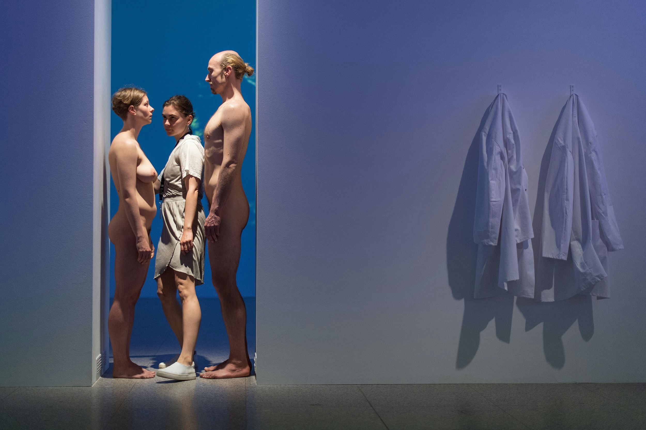 An image of the art installation 'Imponderabilia'. A naked man and woman are standing facing each other in a narrow doorway; a visitor is passing sideways between them.
