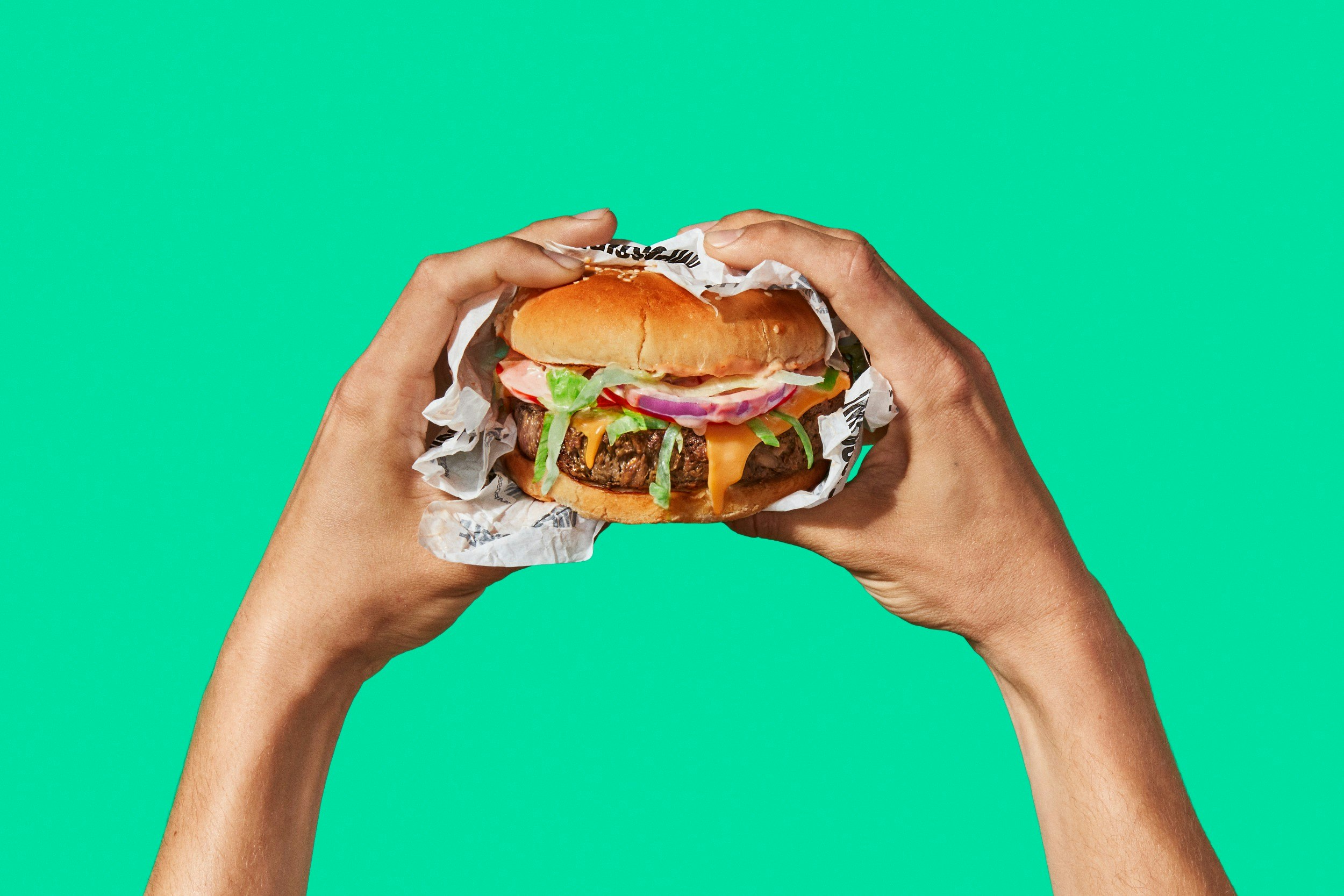 Two hands holding a burger on a green background