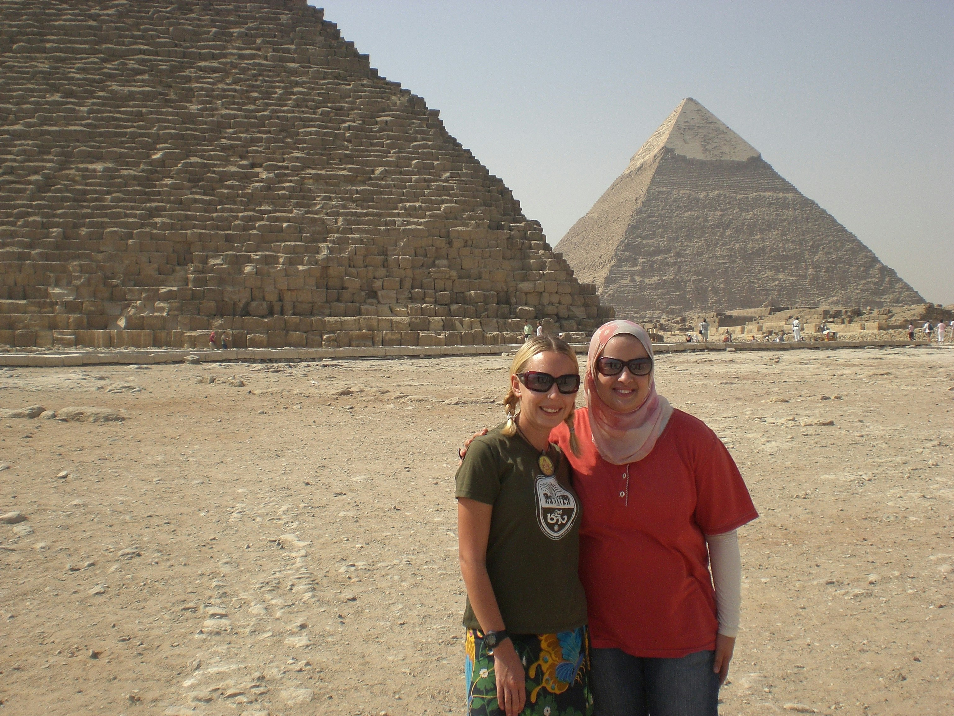 Jess and a headscarf-clad female friend pose in the desert with the sand-coloured Pyramids of Giza rising into the sky behind them.
