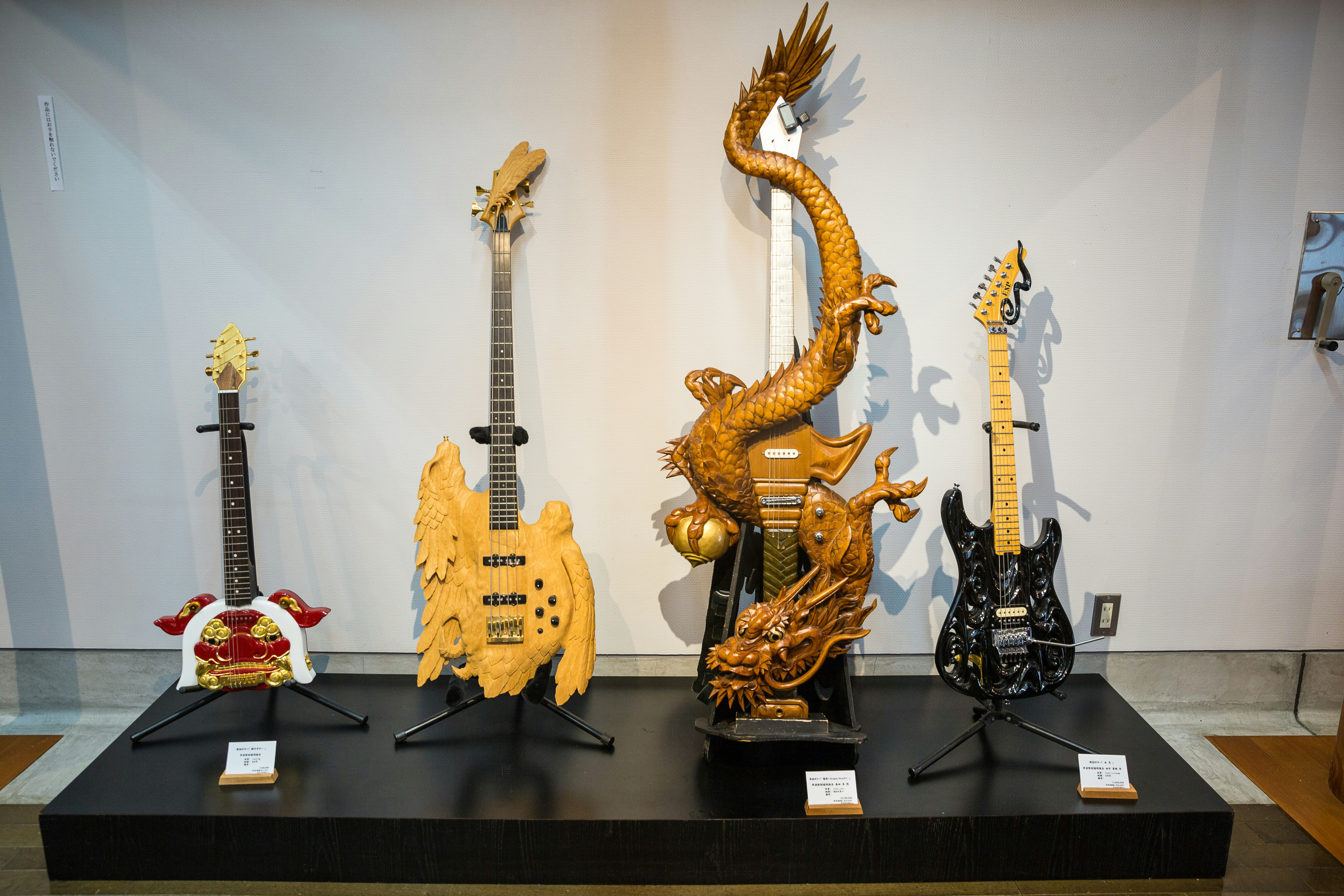 Four electric guitars lean on stands, each with intricate wooden designs. One is an elaborate dragon which goes all the way up the neck of the guitar