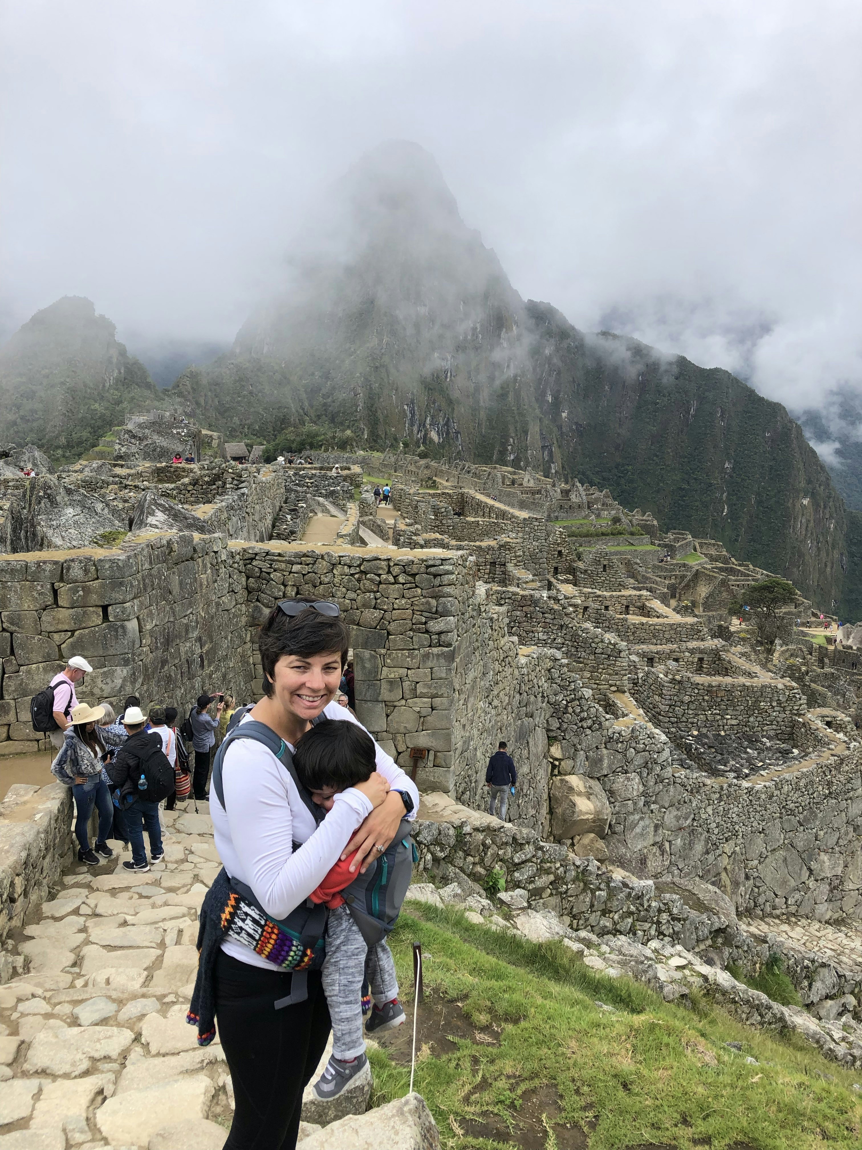 A woman holding a small baby poses in front of Incan ruins at Machu Picchu