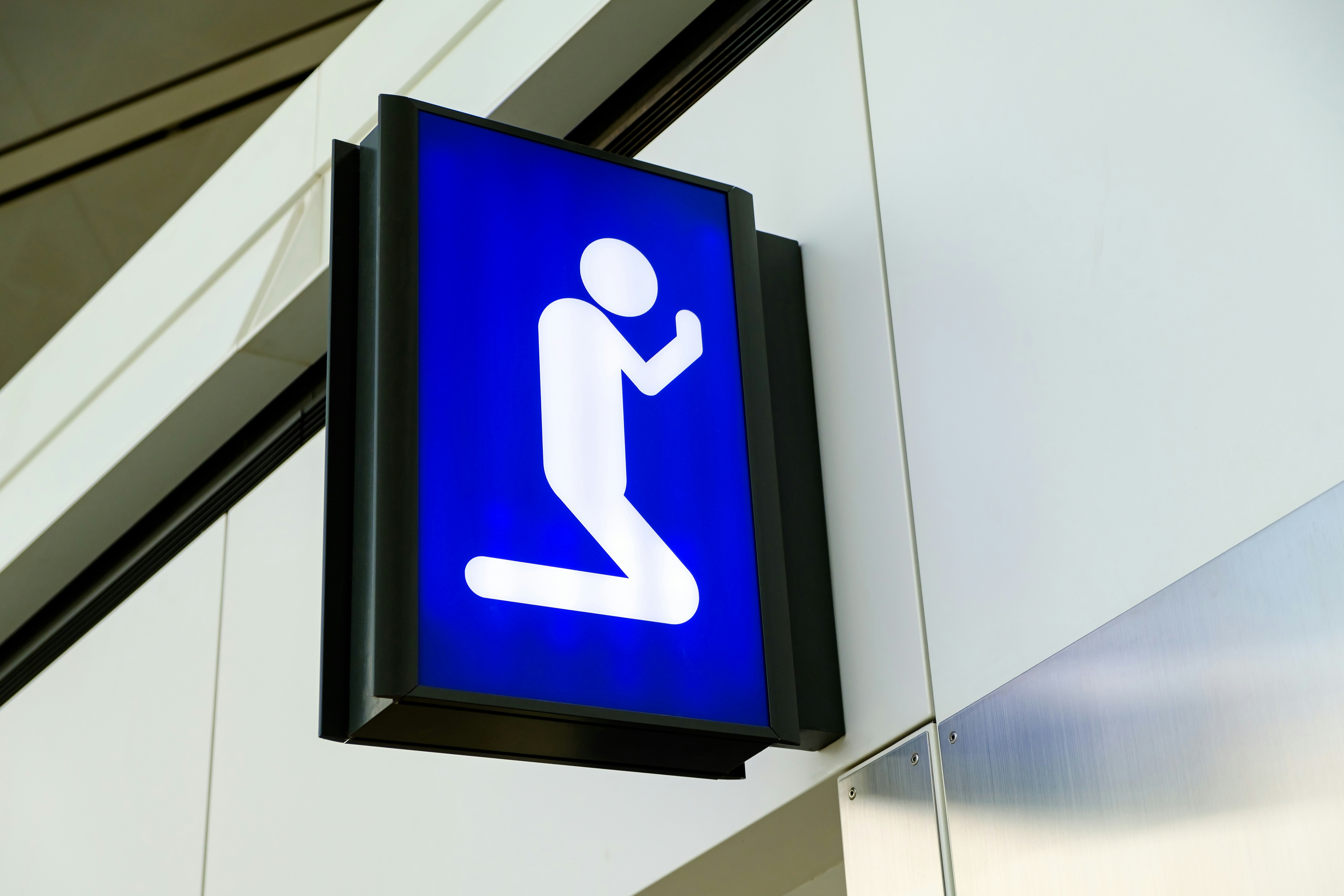 A blue sign with white figure kneeling with its arms raised is on display at an airport