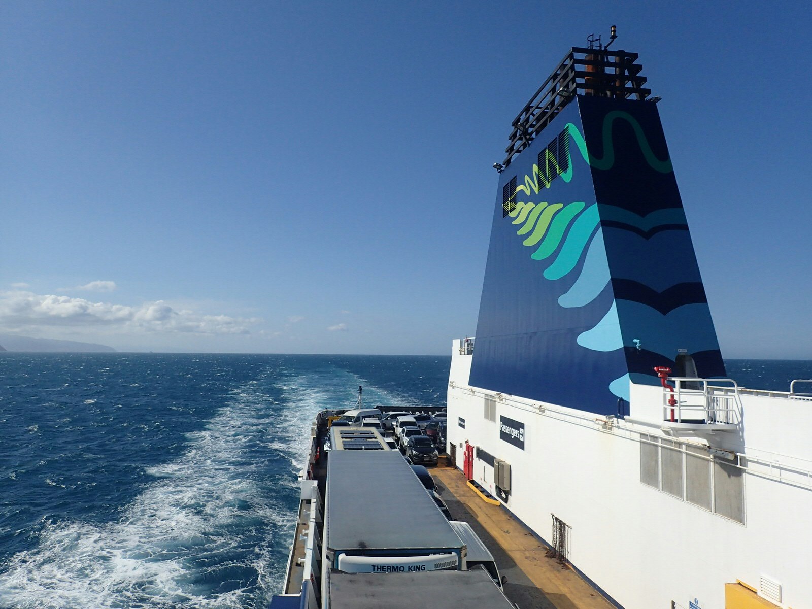Interislander ferry crossing Cook Strait, New Zealand on a clear day. The photo shows the stern of the boat, churning a white trail through the blue sea.
