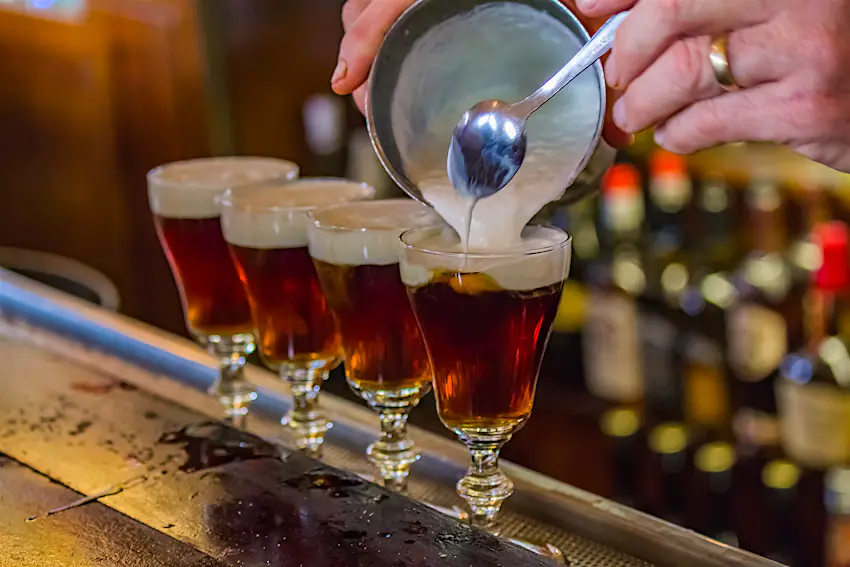Irish Coffee - destination drinks.jpg A bartender tops off the fourth and final glass in row of Irish Coffees on a bar.