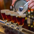 A bartender tops off the fourth and final glass in row of Irish Coffees on a bar. 