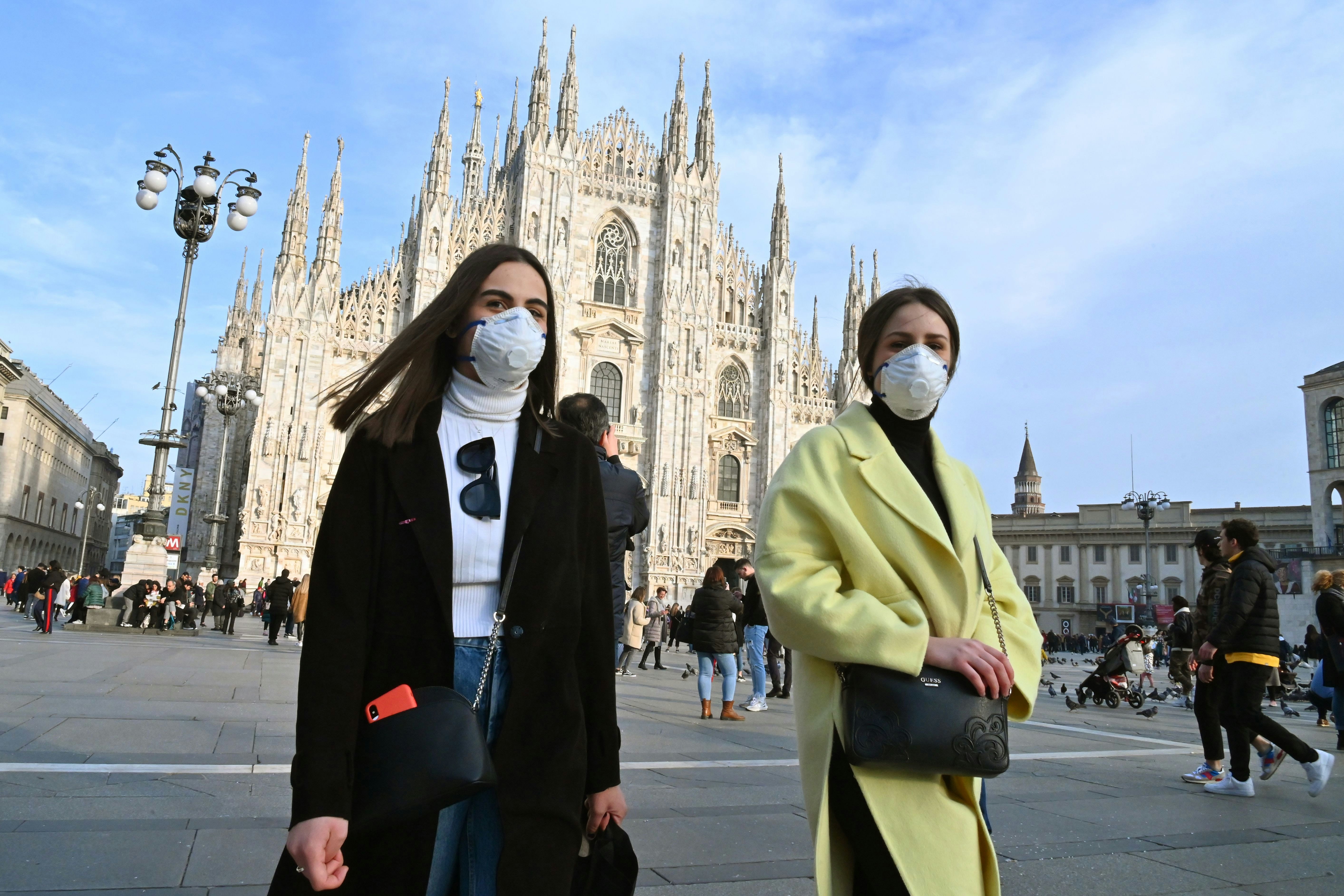 Women wearing face masks walk across Piazza del Duomo in central Milan during the COVID-19 pandemic.