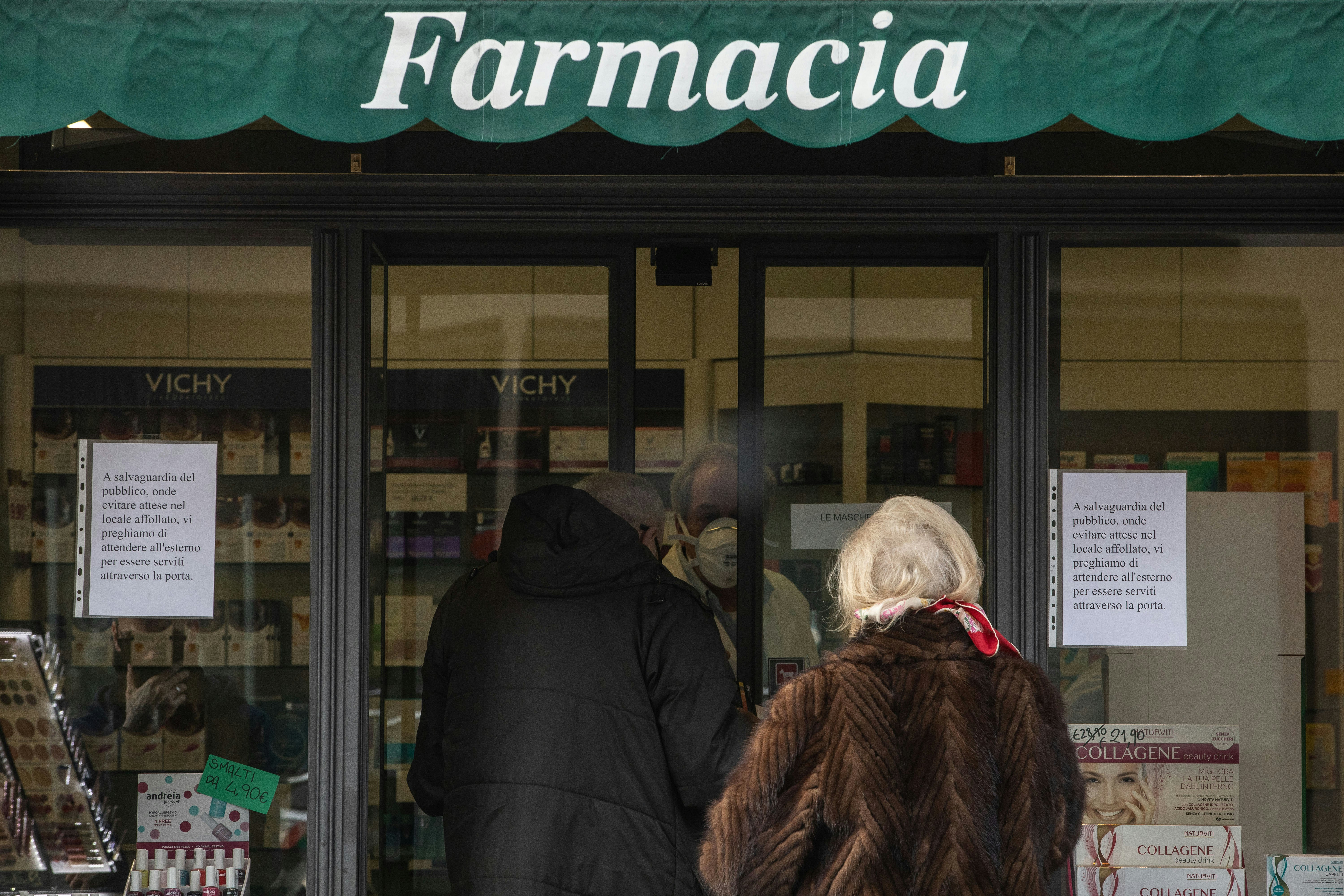 People wearing face masks queue outside a pharmacy in Italy