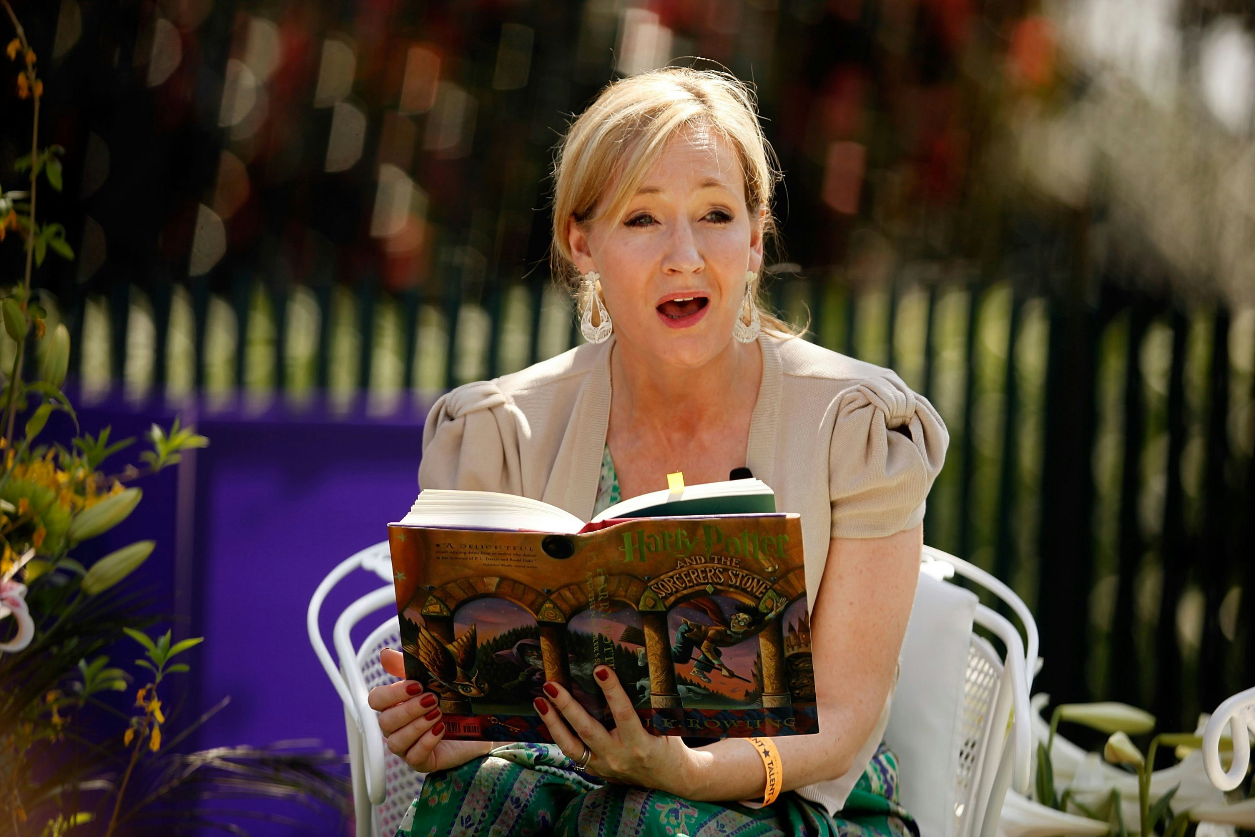 JK Rowling reading a Harry Potter boo while sitting on a bench