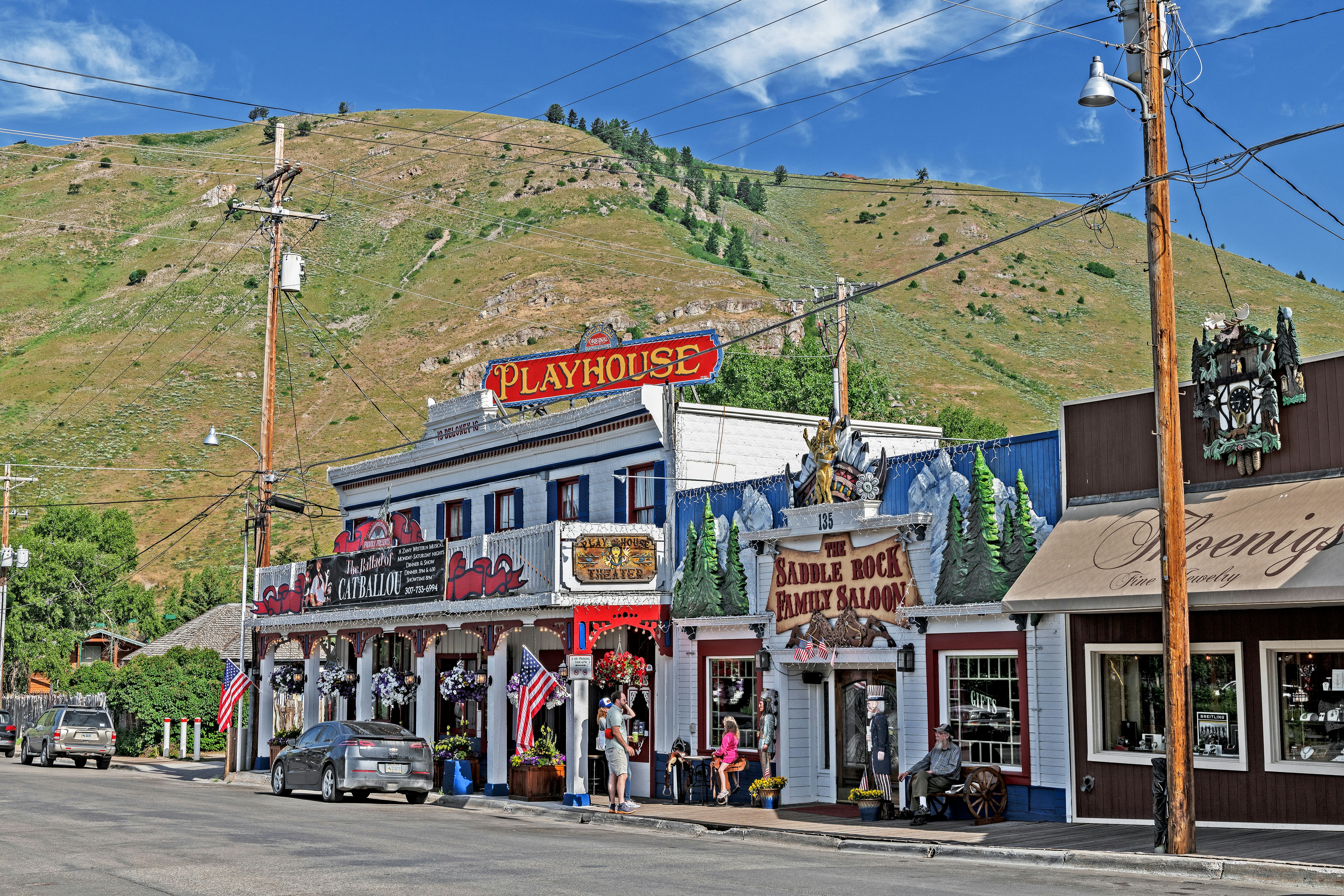 Exteriörvy av Jackson Hole Playhouse är en gammal salong i westernstil.  Det finns en stor grön kulle i bakgrunden. 