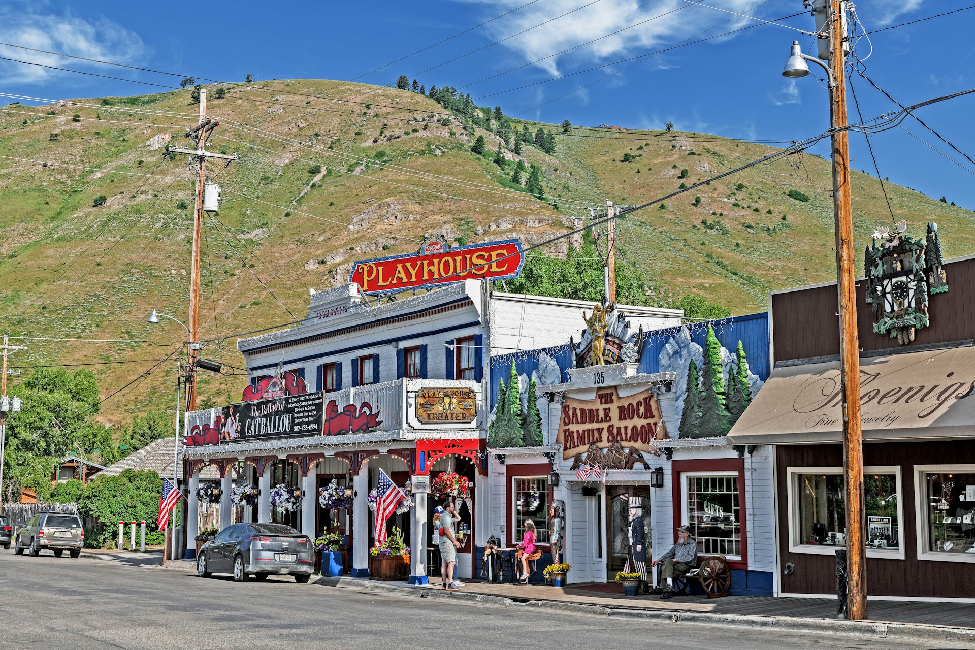 Exterior view of Jackson Hole Playhouse is an old western-style saloon. There is a large green hill in the background. 