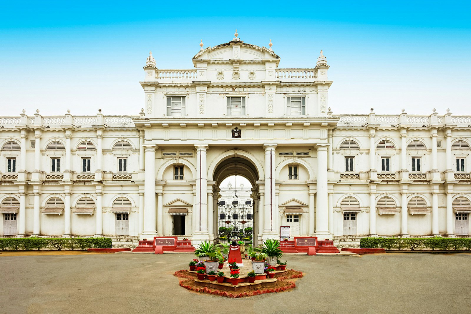 The entrance of the white Jai Vilas Palace; the exterior is covered in columns and arches, and a small garden sits in the foreground. Madhya Pradesh, India.