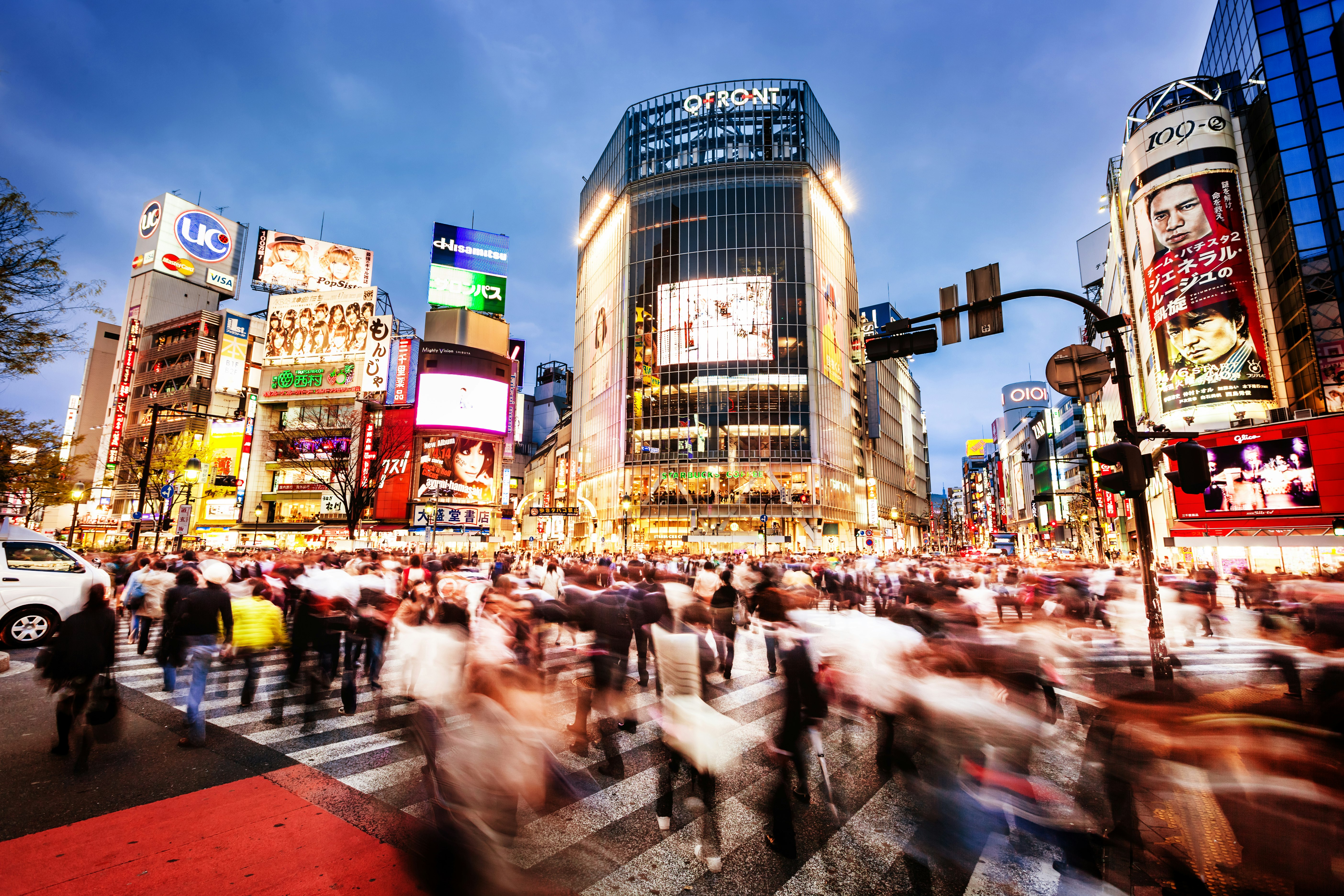Long exposure of pedestrians crossing the famous Shibuya Crossing in Tokyo at dusk.