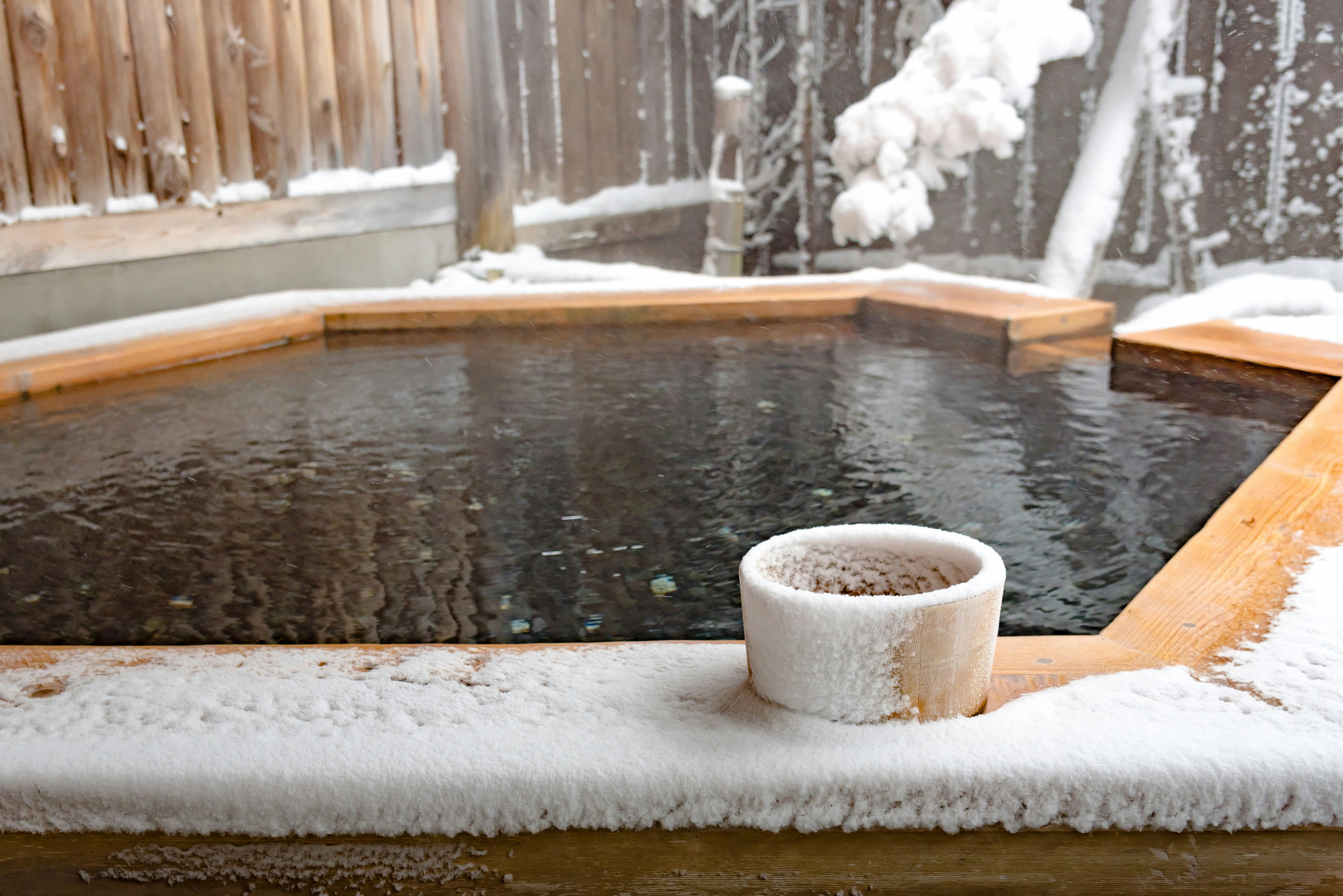 A traditional wooden Japanese outdoor onsen, which is surrounded by snowy countryside.