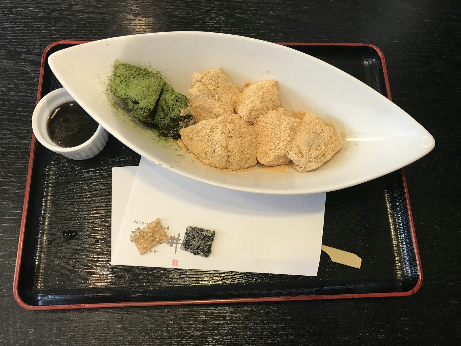 Japanese warabimochi flavoured with green tea and kinako, a traditional Japanese dessert, served in a white dish on a black tray