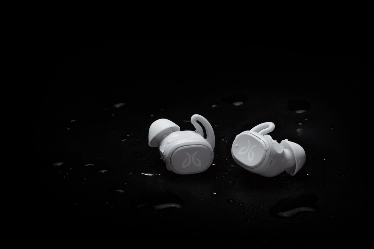 A pair of white Jaybird Vista wireless headphones with drops of water on a black background