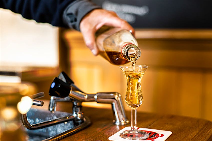 Jenever τζιν, Άμστερνταμ Ένας μπάρμαν στο Άμστερνταμ ρίχνει το jenever/genever σε ένα ποτήρι τουλίπας, ως μέρος μιας παράδοσης που ονομάζεται kopstootje.